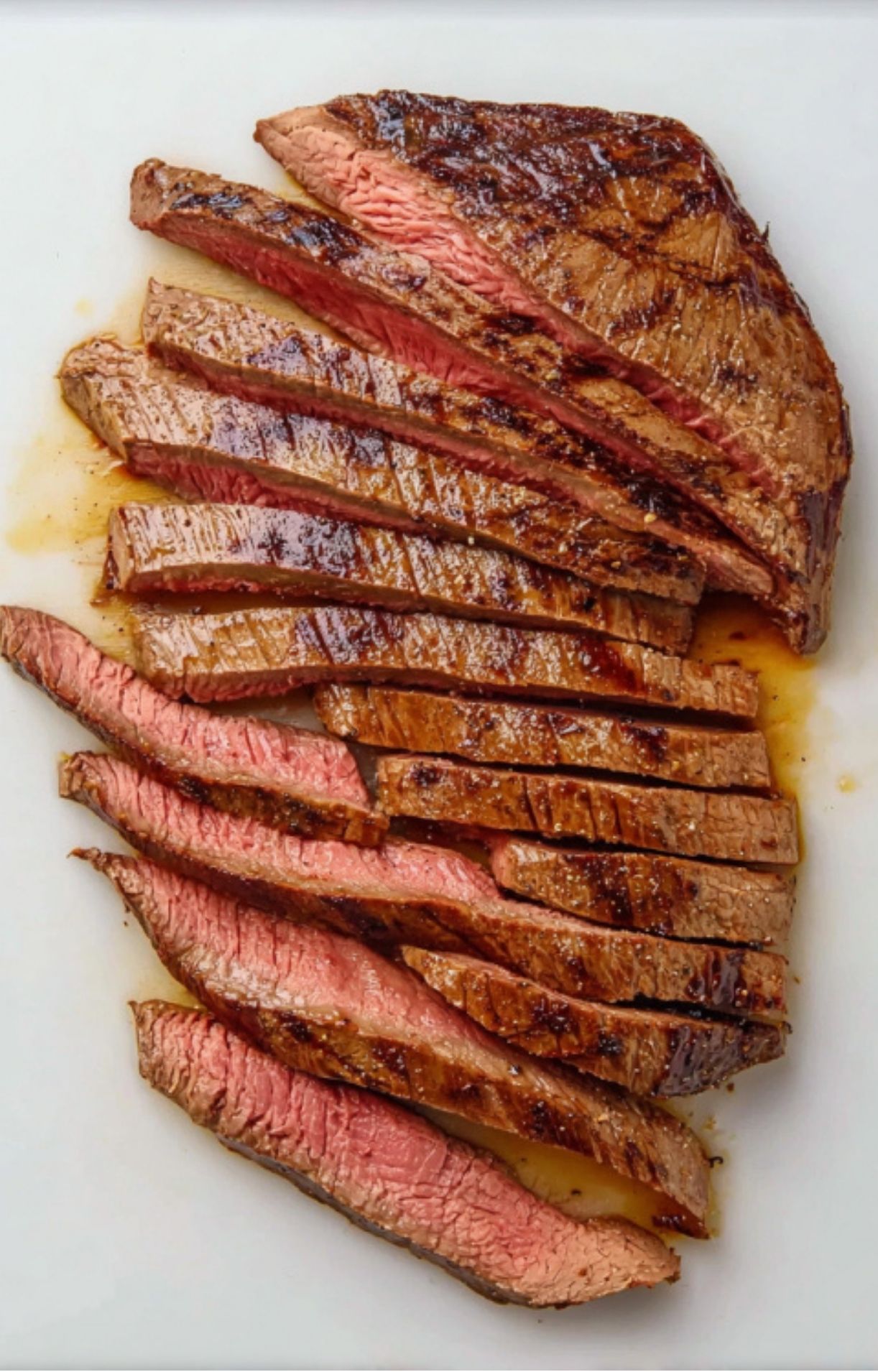 Perfectly cooked and juicy grilled steak sliced thin on a white cutting board, showing a pink medium-rare center.