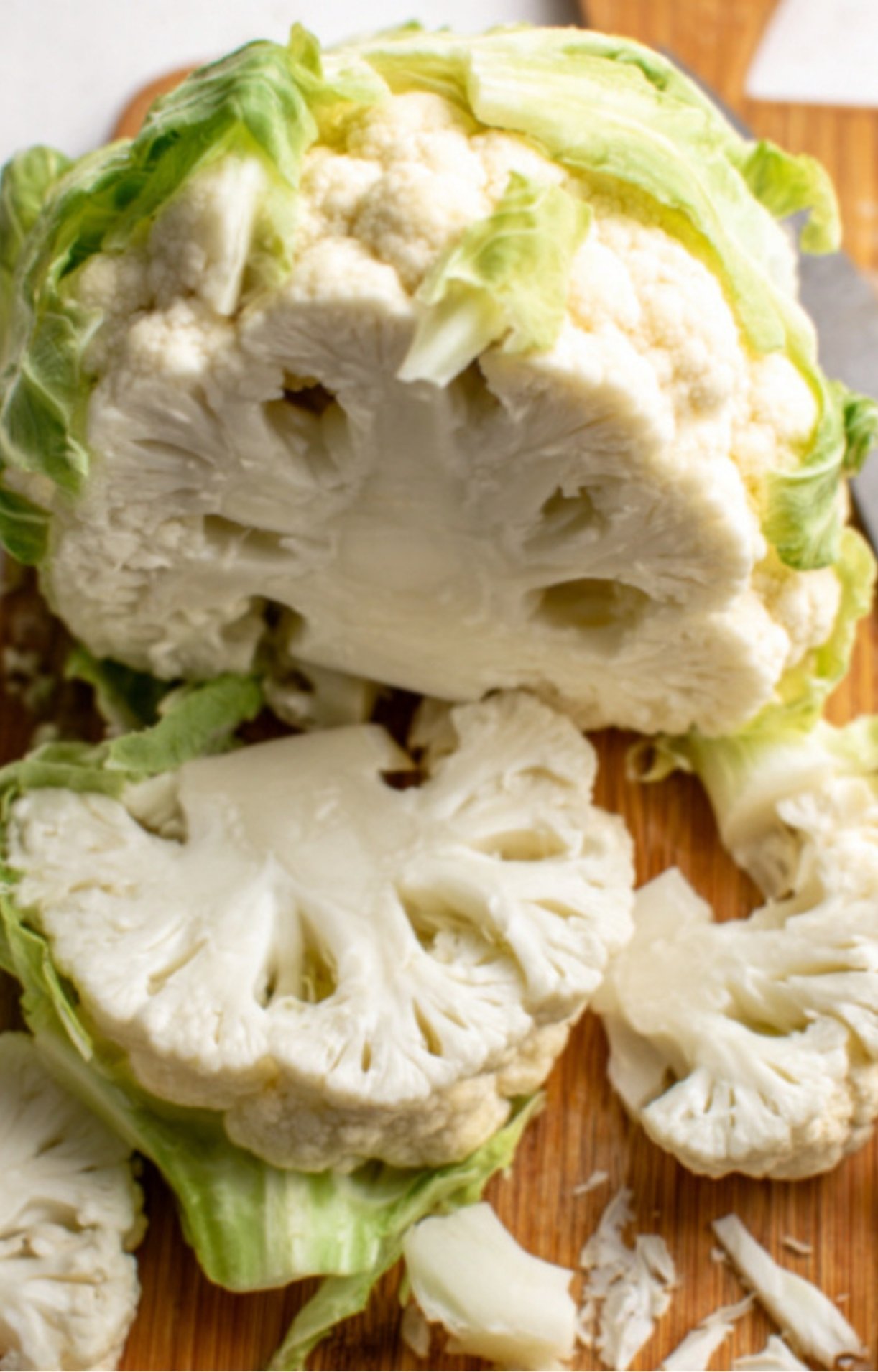 Head of cauliflower being sliced into thick pieces on a wooden board for making cauliflower steaks.
