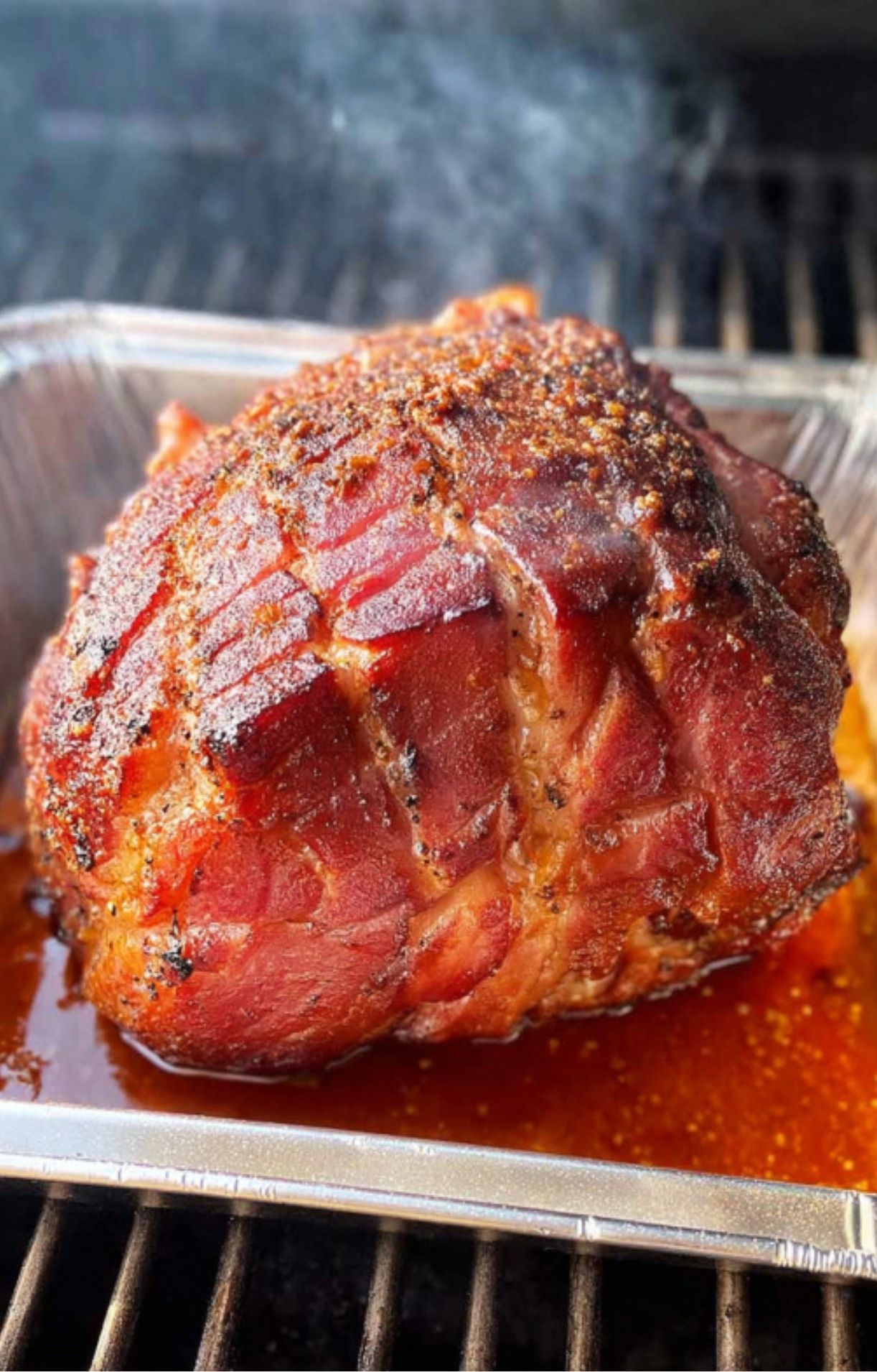 Ham roasting in a foil pan on a pellet grill, seasoned and smoking for deep flavor.