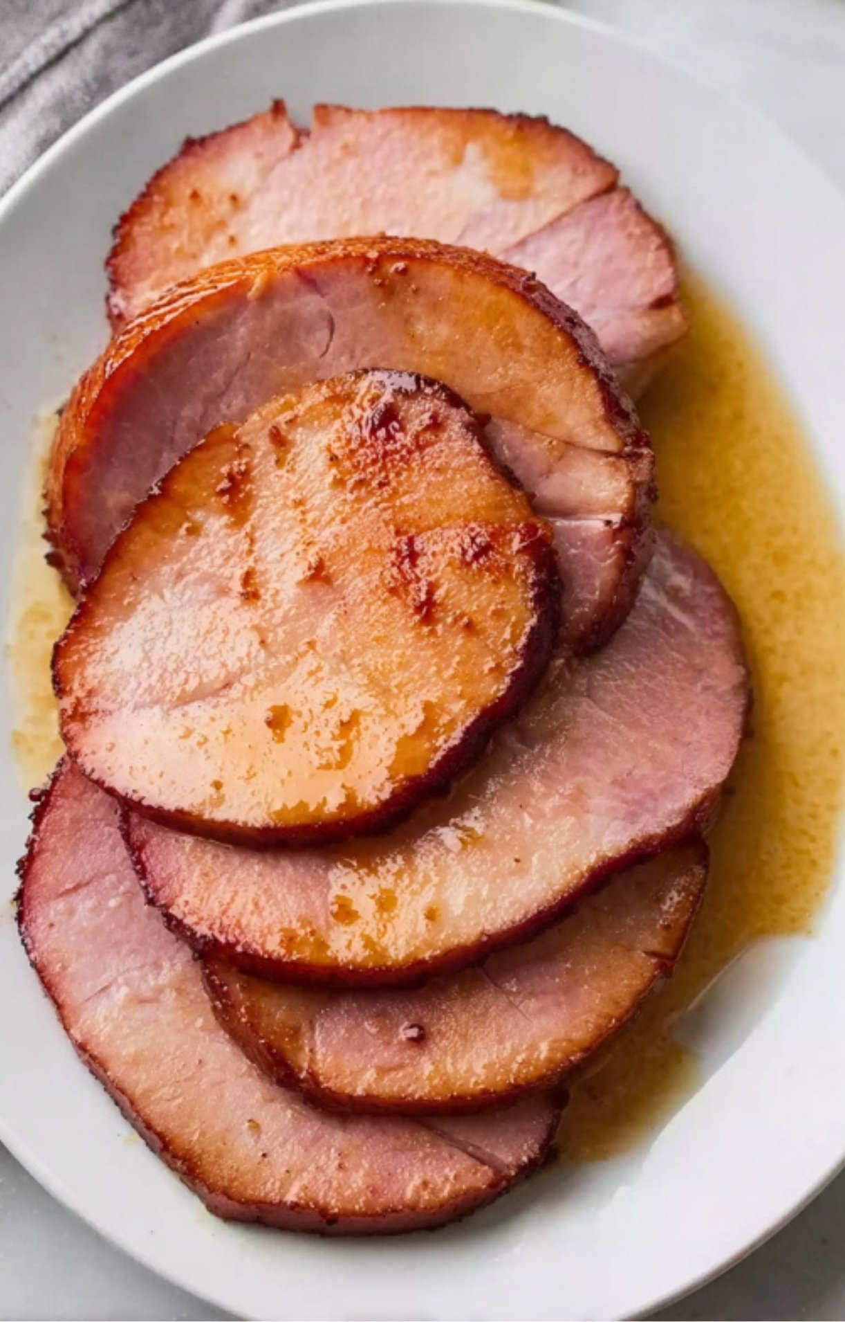 Sliced ham on white plate with pan juices, moist and ready to serve for family dinner