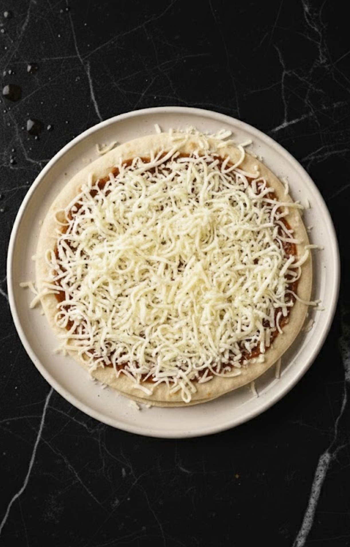 A thick layer of shredded white mozzarella cheese covering the sauce-topped pizza base.