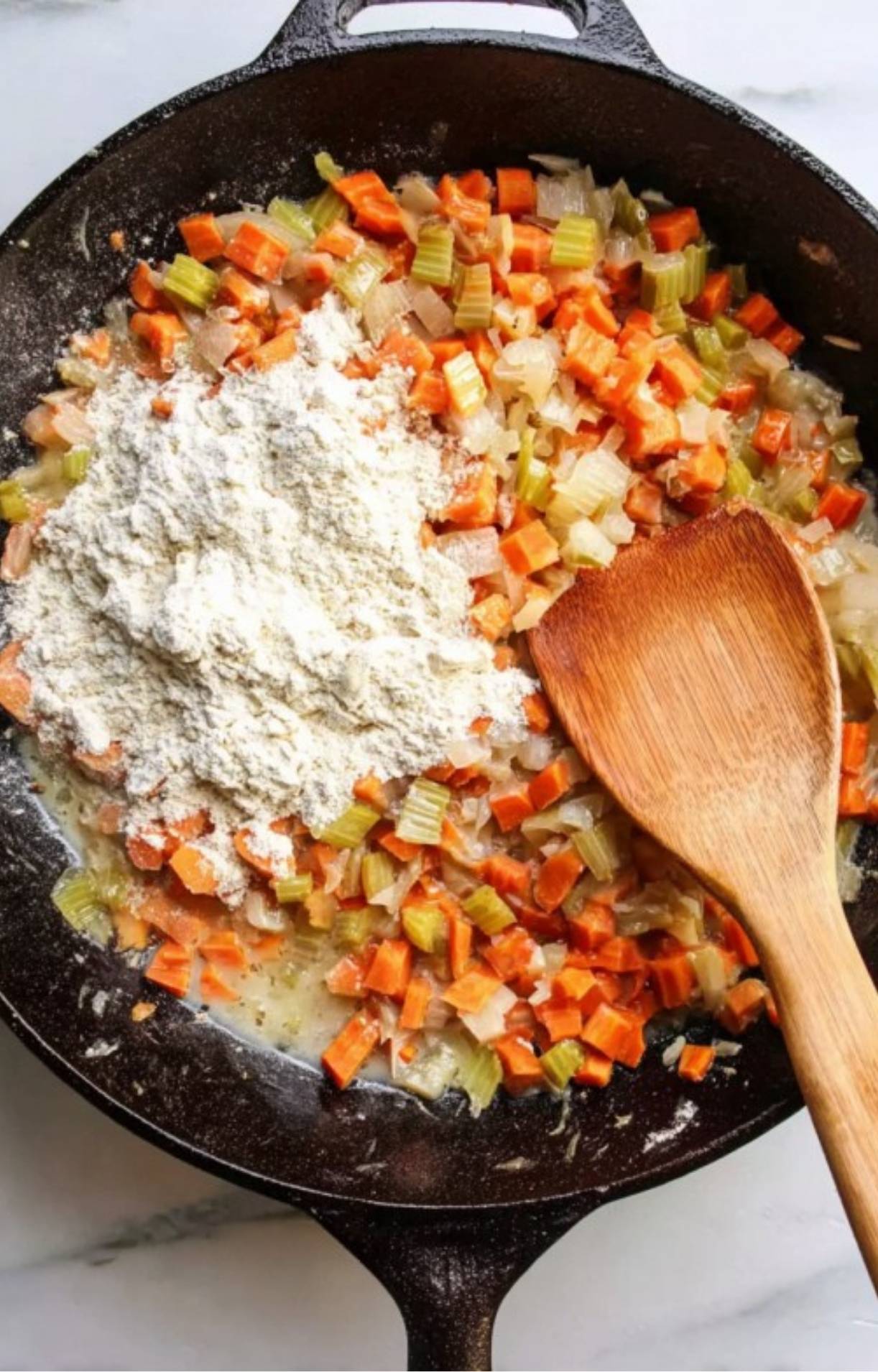 A pile of white flour being stirred into the sautéed vegetable mixture to thicken the Turkey Pot Pie with Puff Pastry.