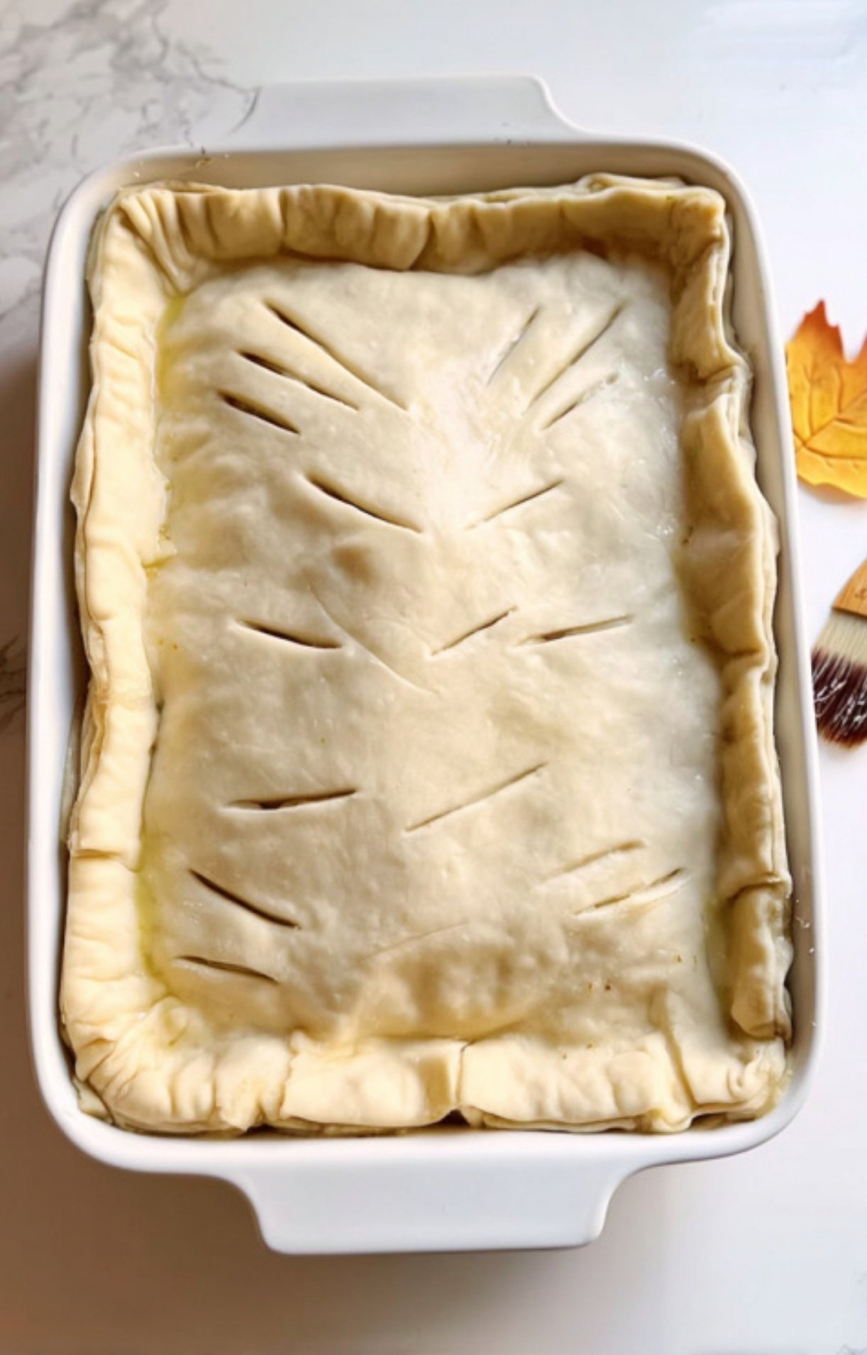 A sheet of raw crescent roll dough draped over the filling with decorative vent slits cut into the top.