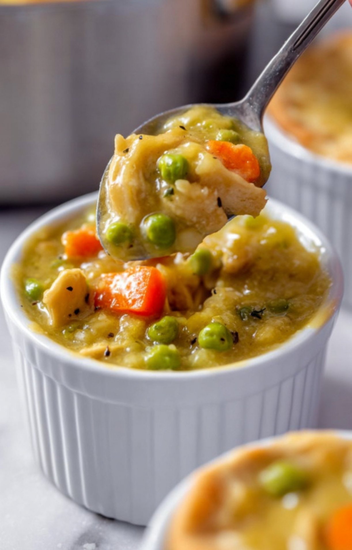 A spoon lifting a portion of thick, savory turkey and vegetable filling out of a white ramekin to show the hearty texture.