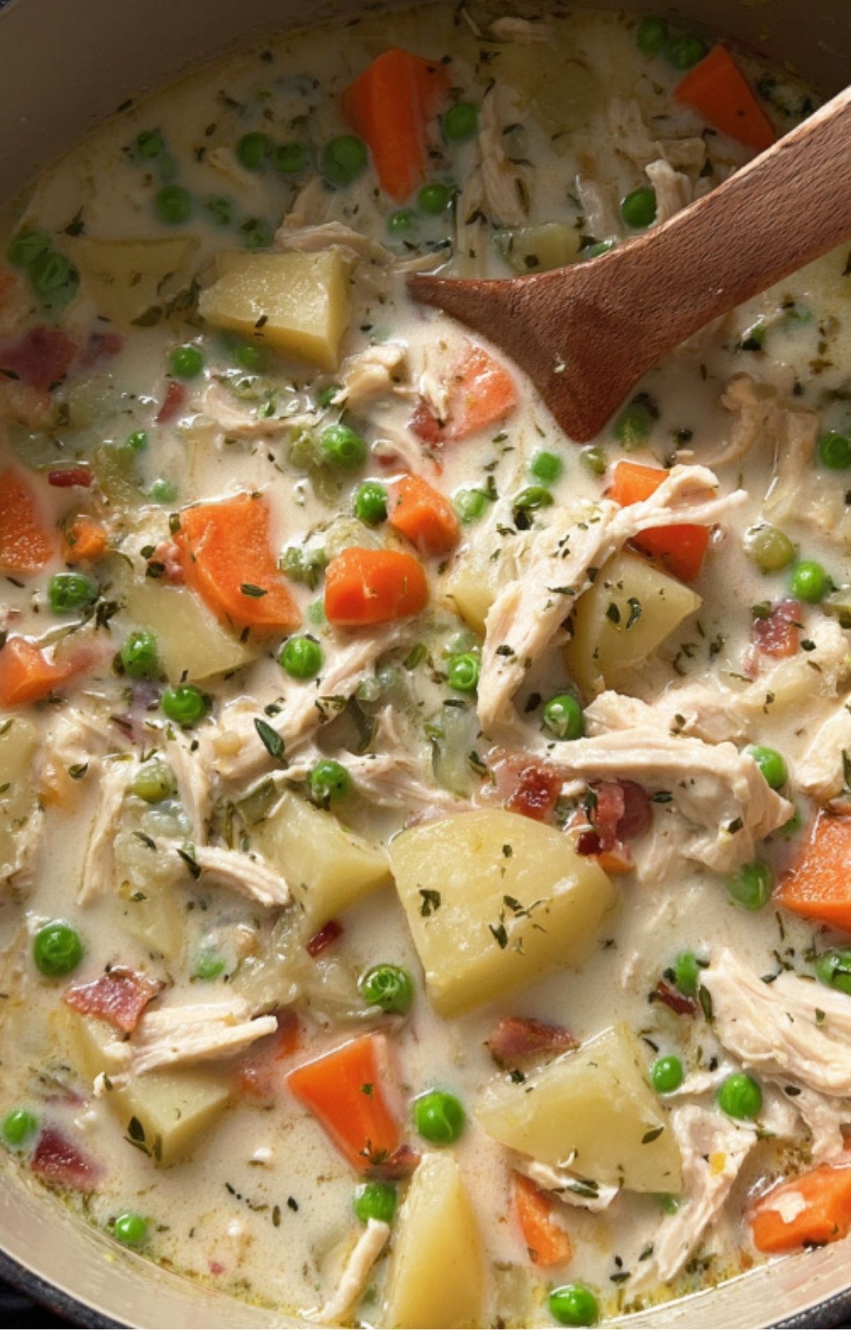 An overhead close-up of turkey pot pie soup simmering in a pot, showing chunks of orange carrots, green peas, and tender turkey in a rich, creamy broth.