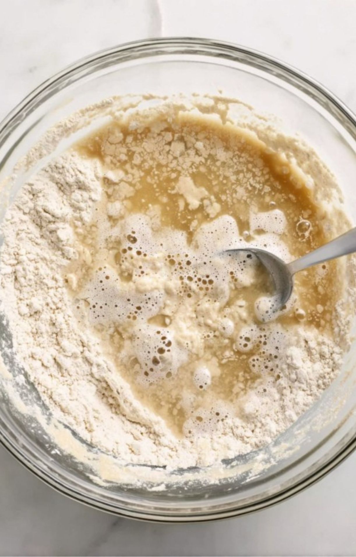 Mixing wet ingredients into dry flour in a glass bowl with a spoon to create the biscuit dough for a healthy turkey pot pie.