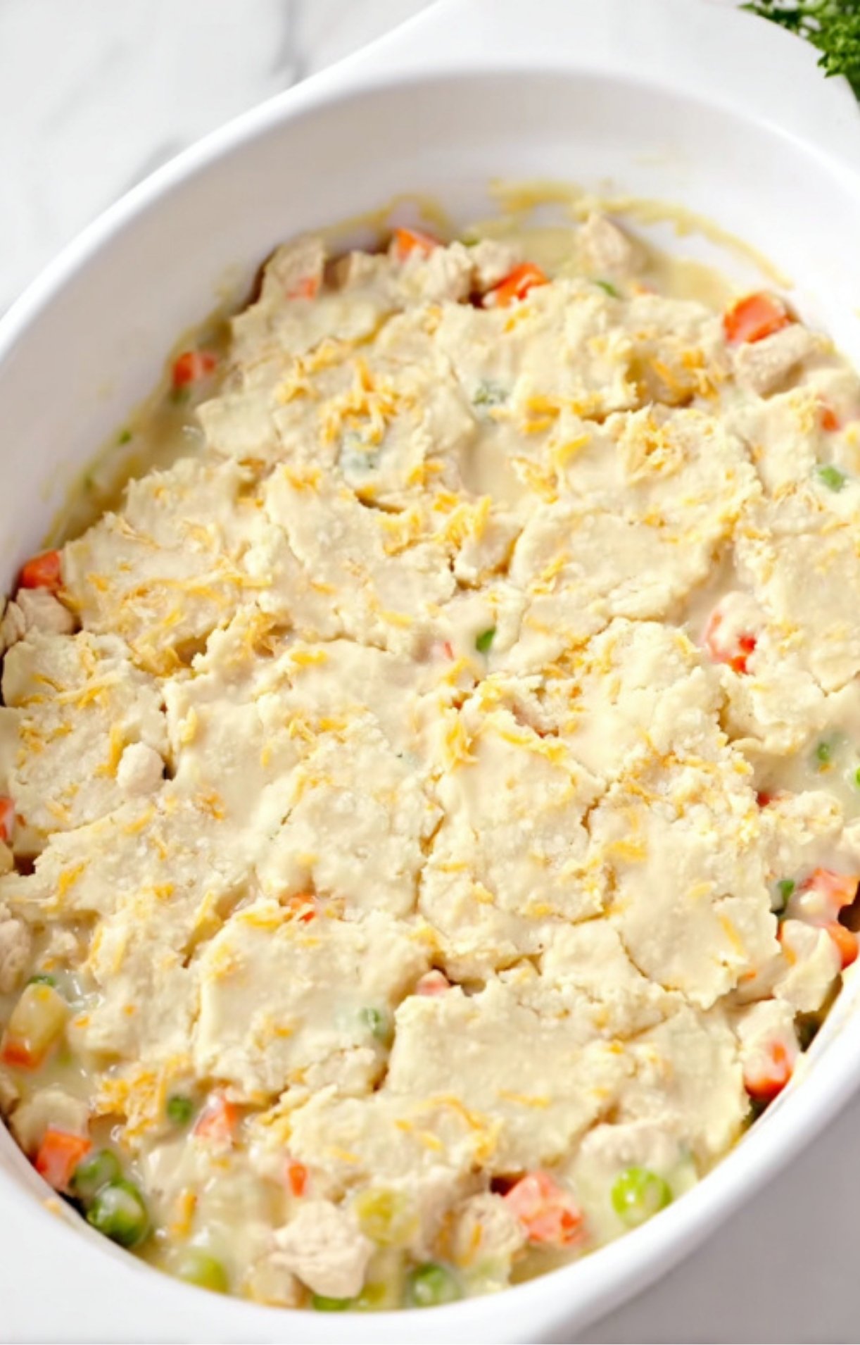 Raw almond flour-based biscuit dough flattened over a creamy turkey and vegetable mixture in a white casserole dish.