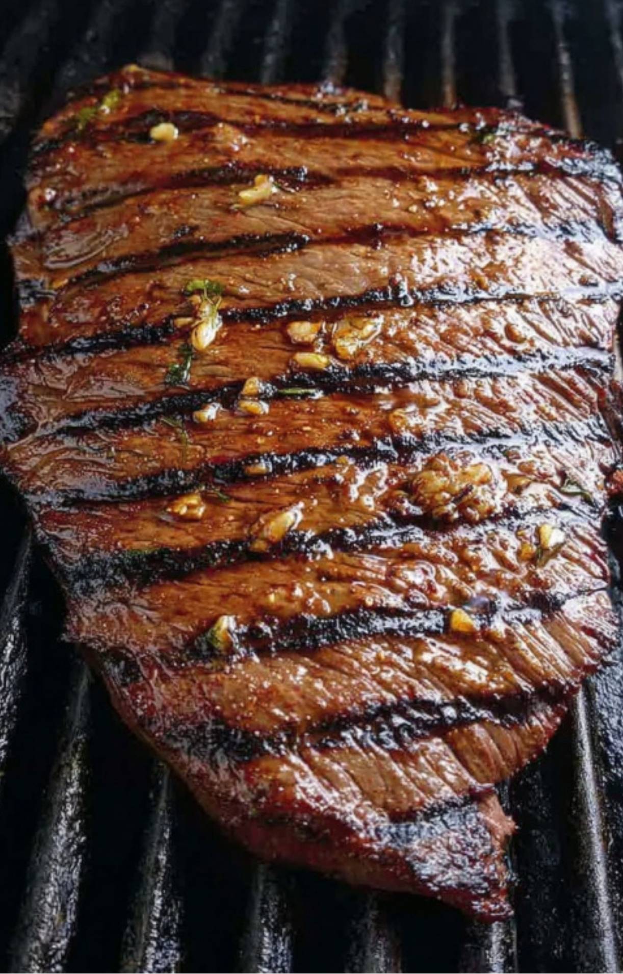 Marinated flank steak sizzling on a grill with perfect sear marks and garlic.