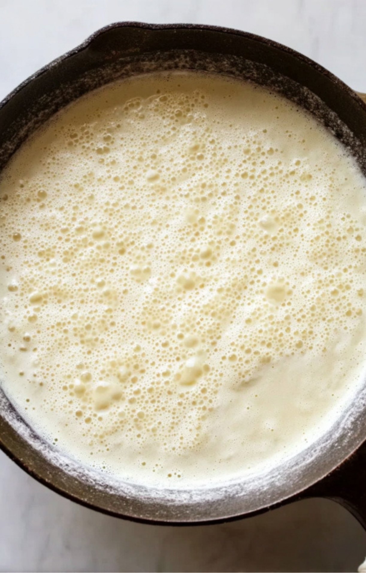 A close-up of a creamy white sauce simmering and bubbling in a cast-iron skillet.