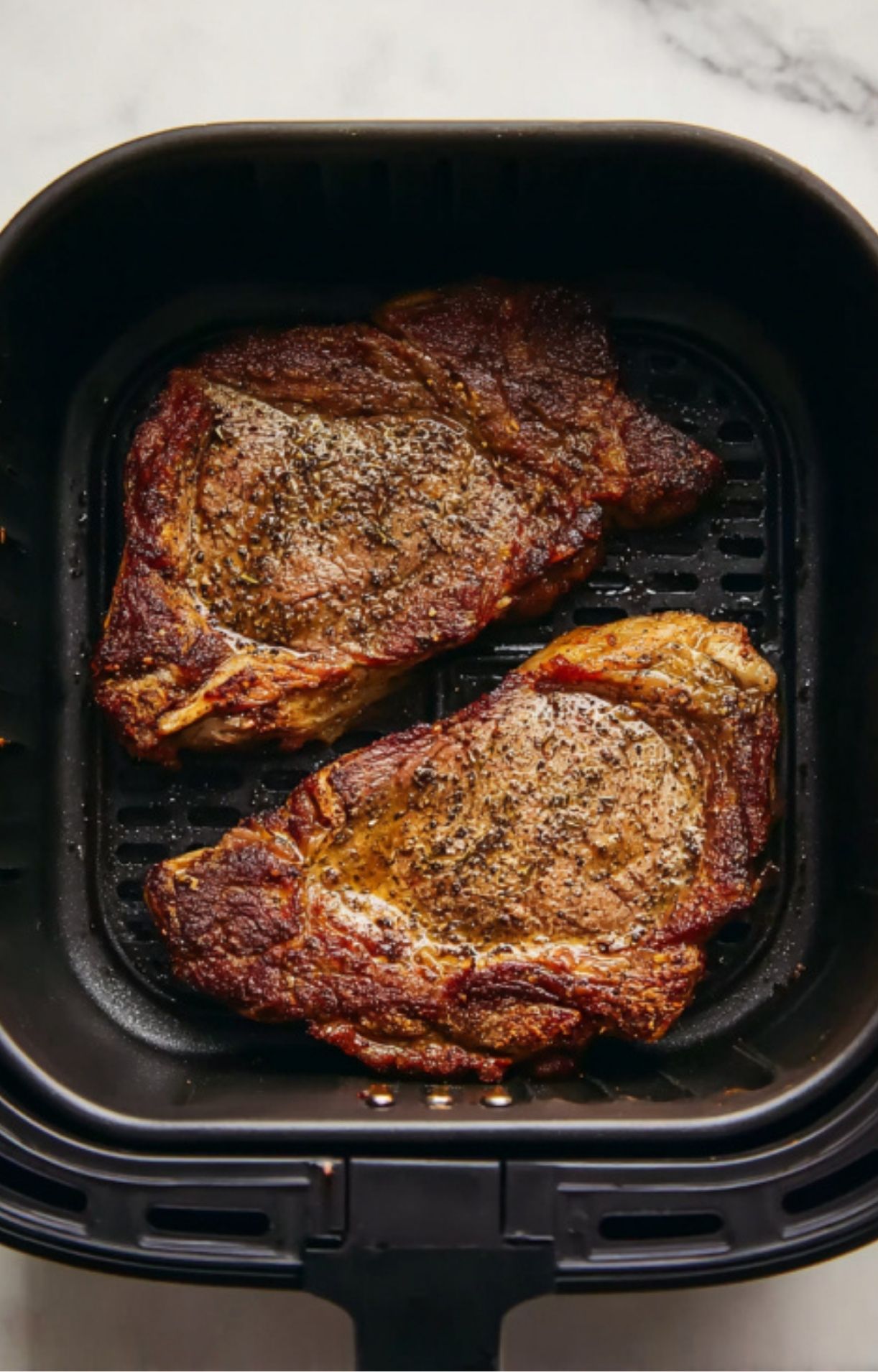 The steaks inside the air fryer showing a developing brown crust after the initial minutes of cooking.