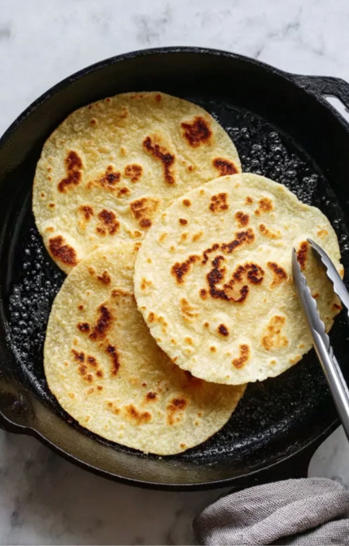 Three corn tortillas browning in a black cast iron skillet, ready to be filled with steak and toppings.