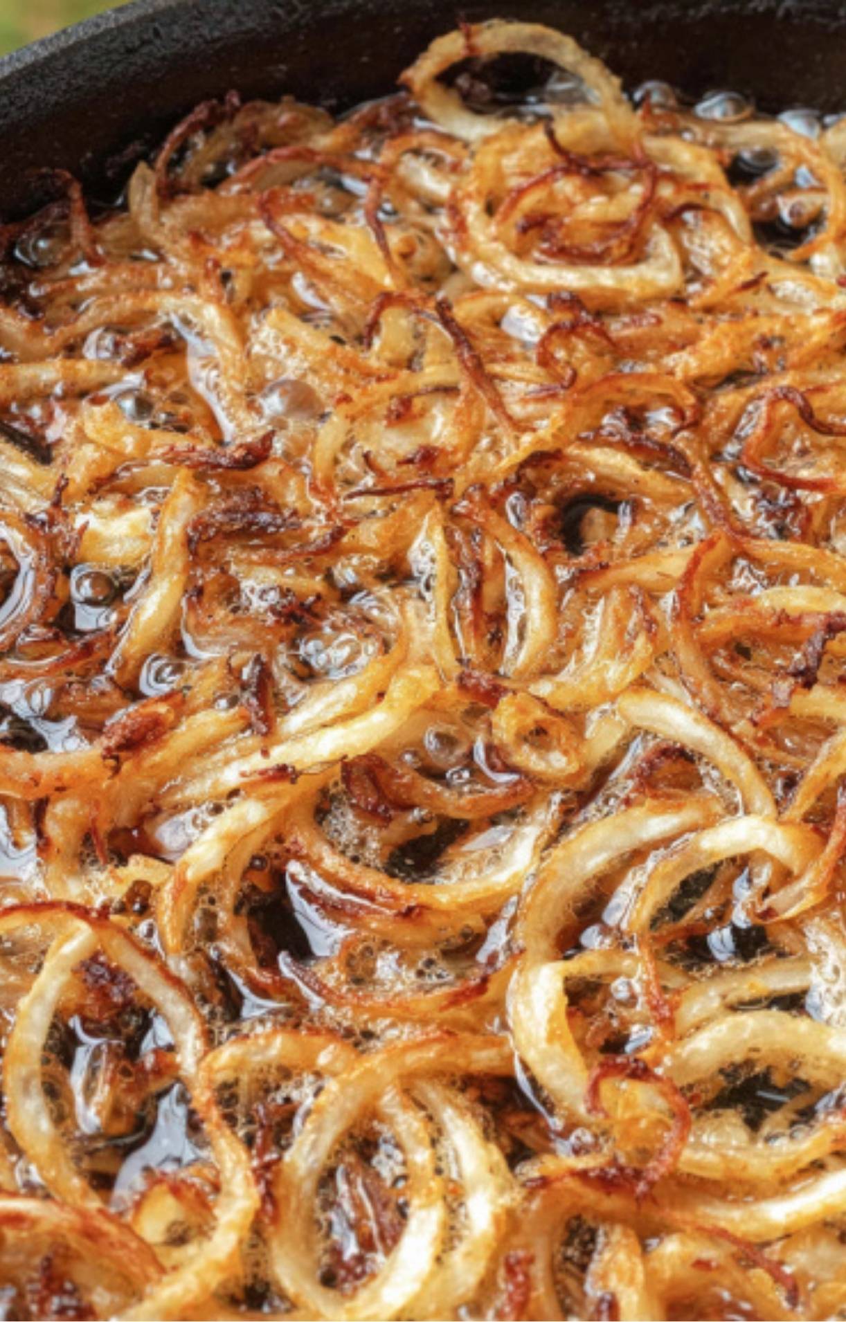 Thinly sliced onions bubbling and crisping in a skillet of hot oil, ready for steak sandwich toppings.