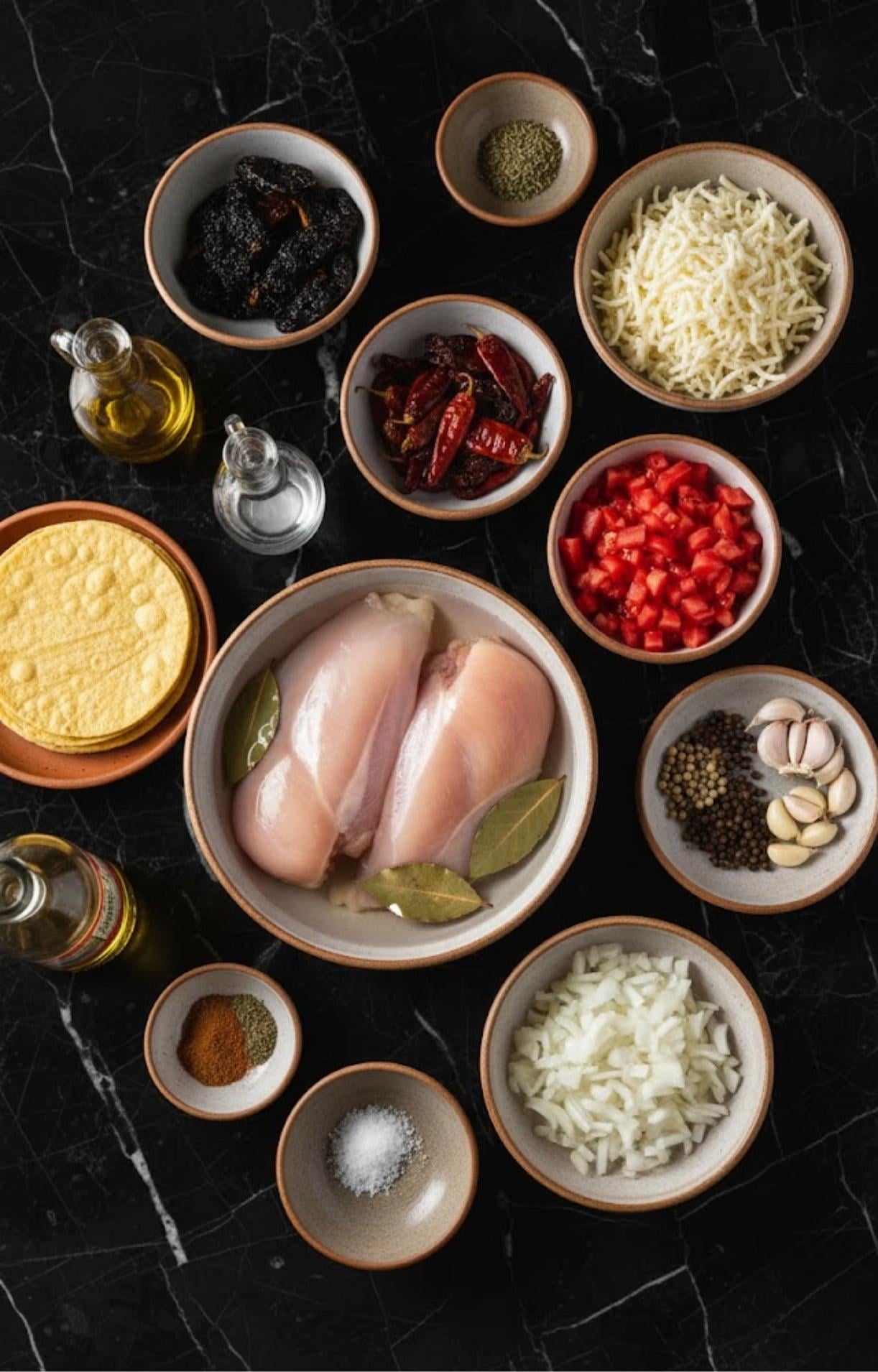 An overhead shot of all ingredients including chicken, dried chilies, spices, tomatoes, onions, and tortillas laid out in small bowls.
