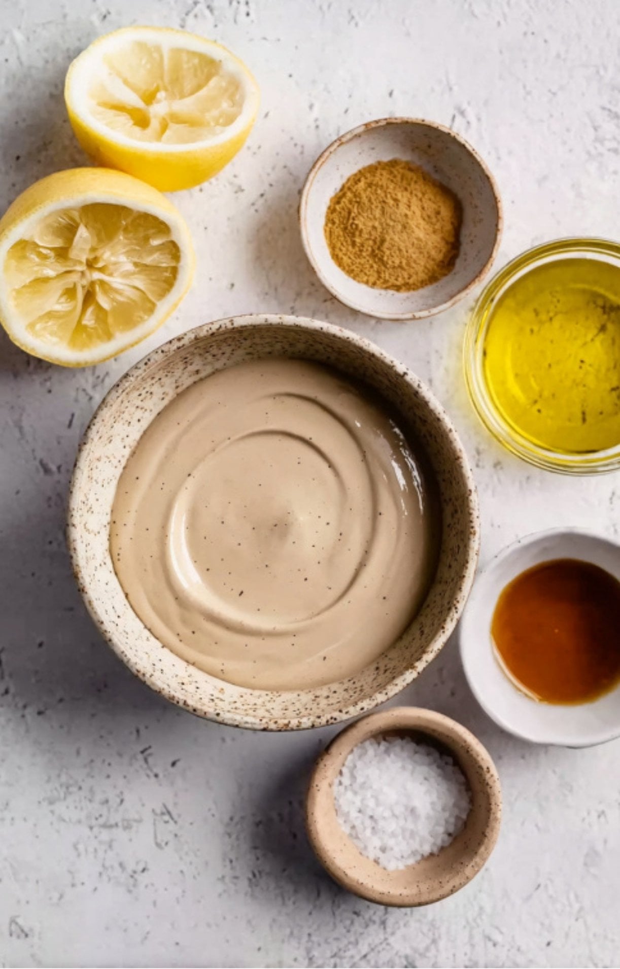 Lemon halves, spices, oil, and a bowl of creamy tahini ready for mixing.