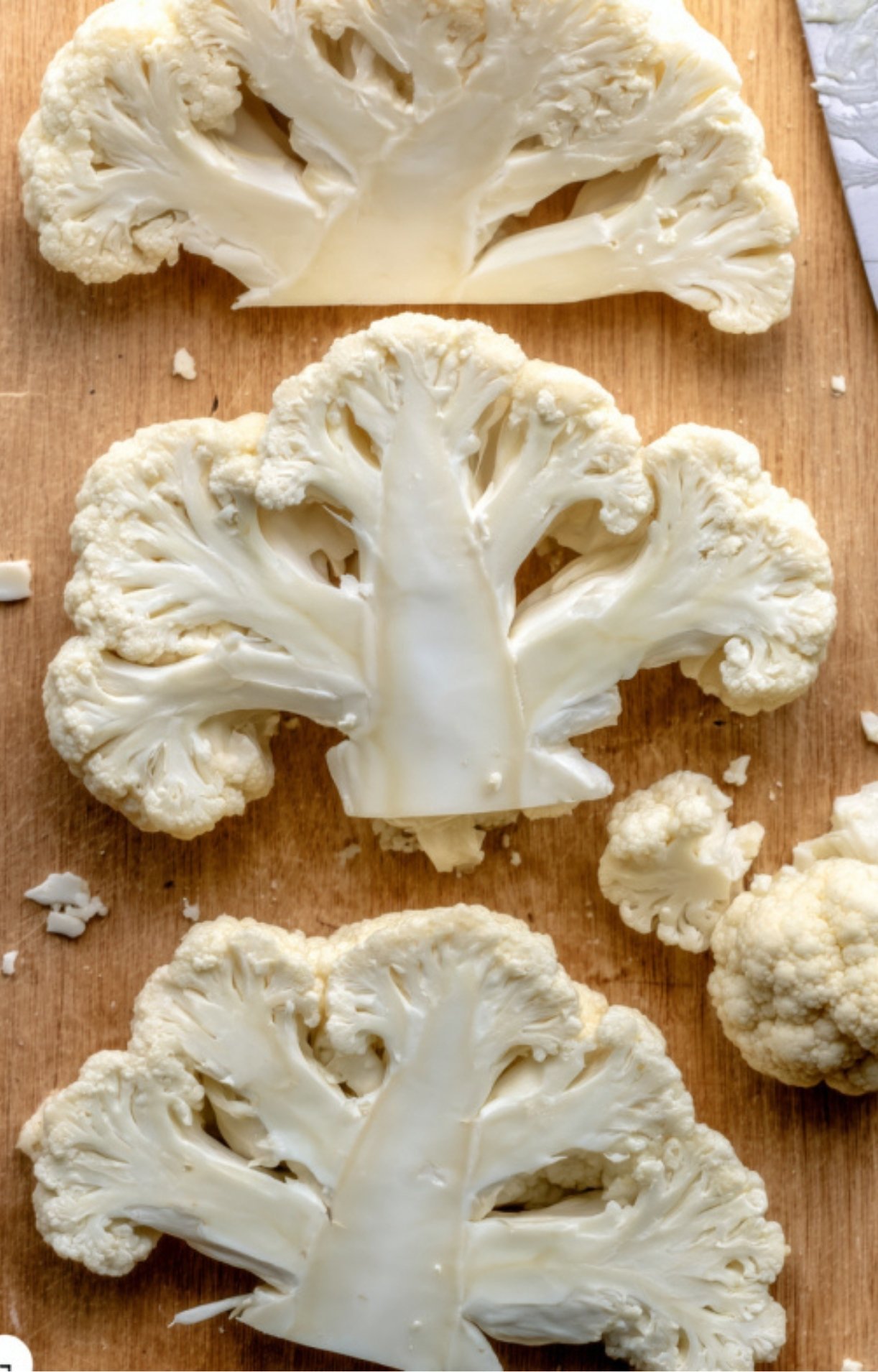 Freshly cut raw cauliflower steaks lined up on a wooden cutting board, ready for seasoning.