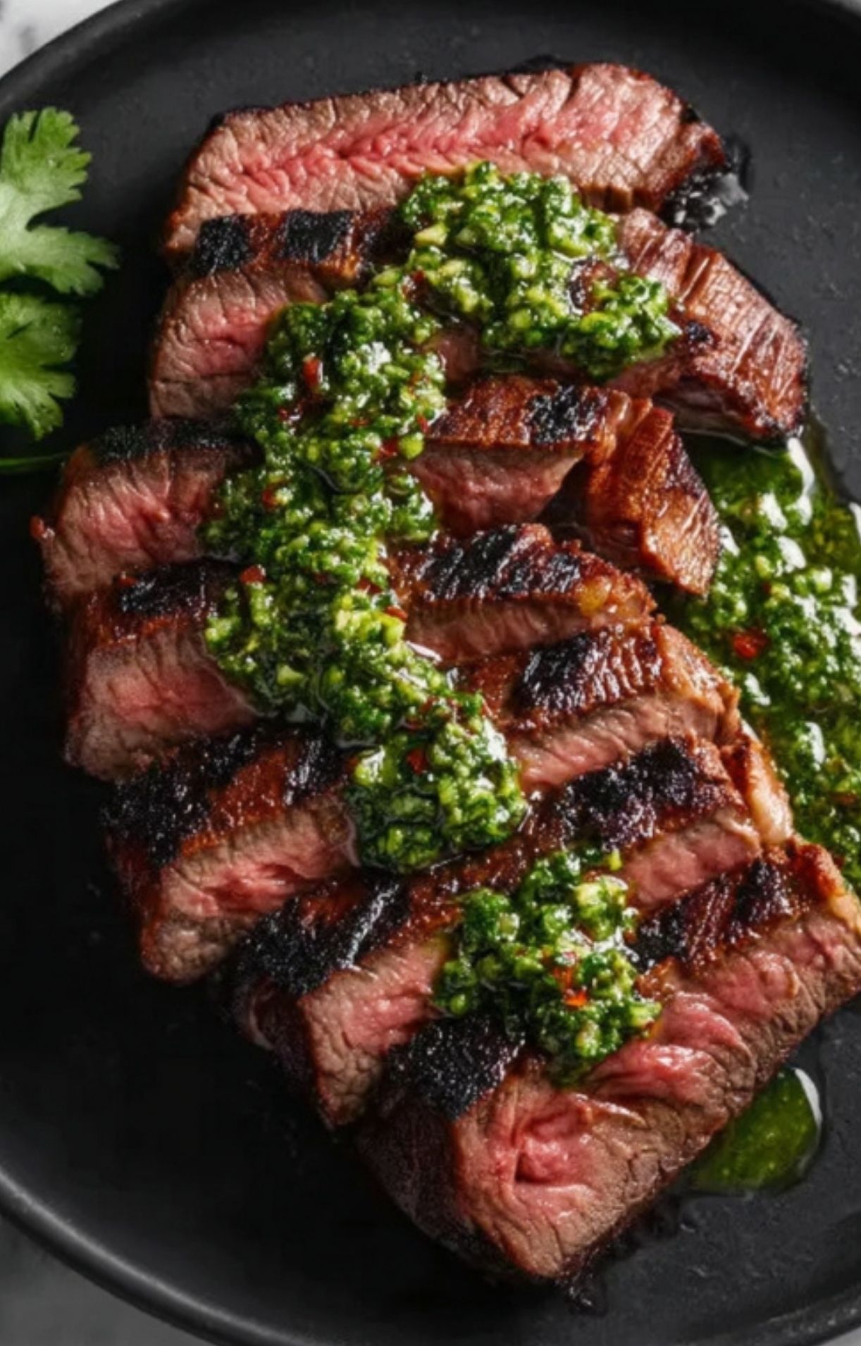 Sliced grilled skirt steak topped with bright green chimichurri sauce on a black plate. Perfect for summer grilling, keto dinners, and high protein meals.