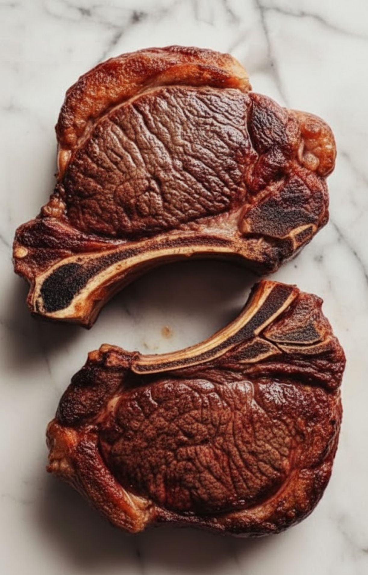 Two grilled bone-in ribeye steaks on marble. Classic steakhouse cuts, perfect for pairing with fresh chimichurri sauce and summer grilling.