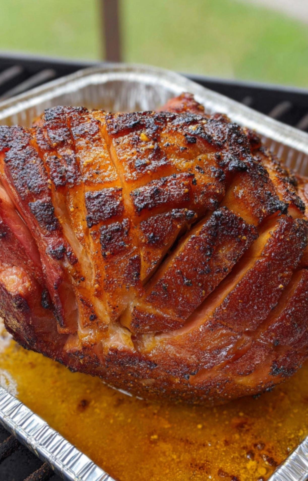 Smoked ham in an aluminum pan on the grill, soaking up flavorful juices while finishing cooking.