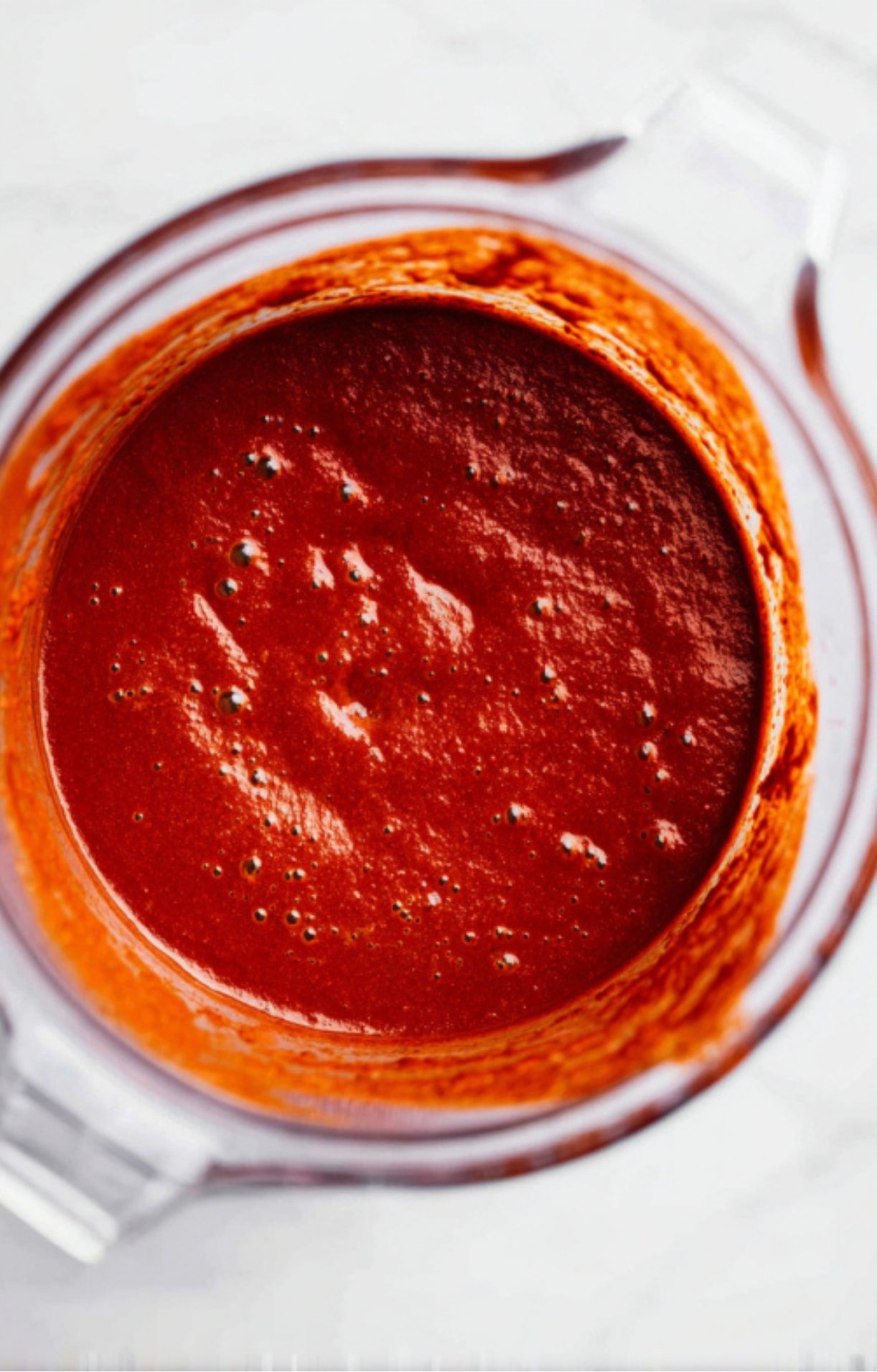 A close-up view of a deep red, smooth chili sauce inside a blender jar.