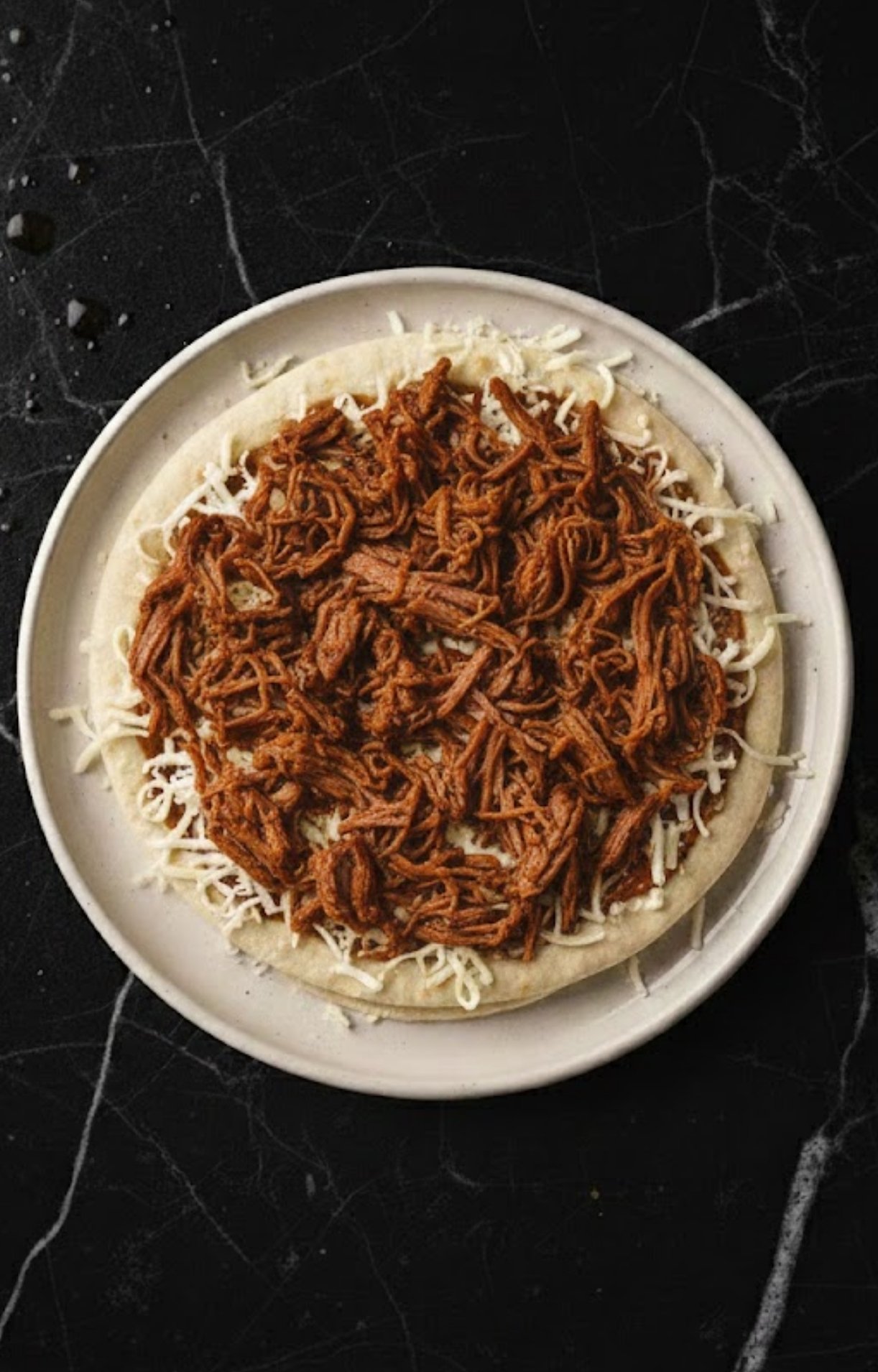 A generous portion of seasoned shredded beef spread over the bed of mozzarella cheese.