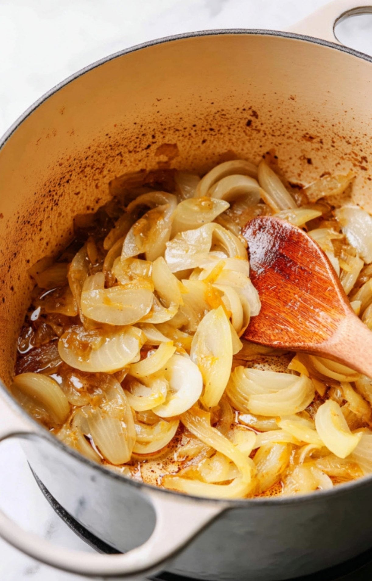 Sliced onions being softened with a wooden spoon in the Dutch oven to create the aromatic base.