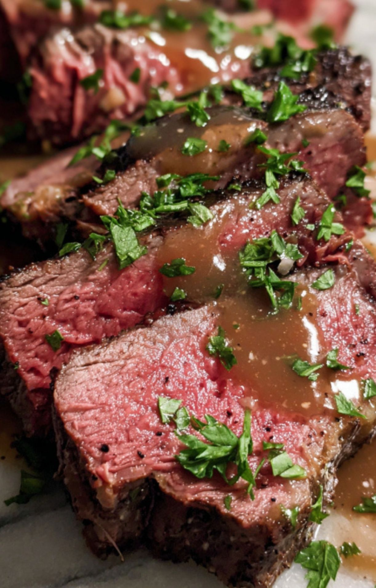 Close-up of medium-rare beef slices topped with rich brown gravy and freshly chopped green parsley.