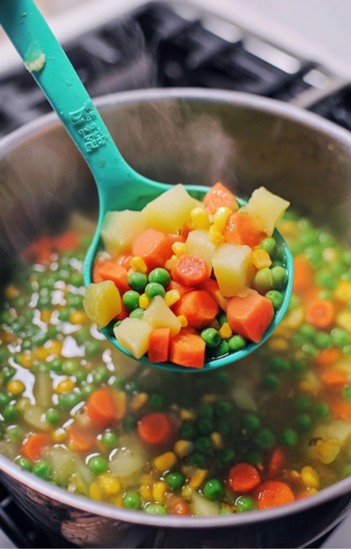 A turquoise ladle scooping out a mixture of boiled potatoes, carrots, peas, and corn from a steaming pot.