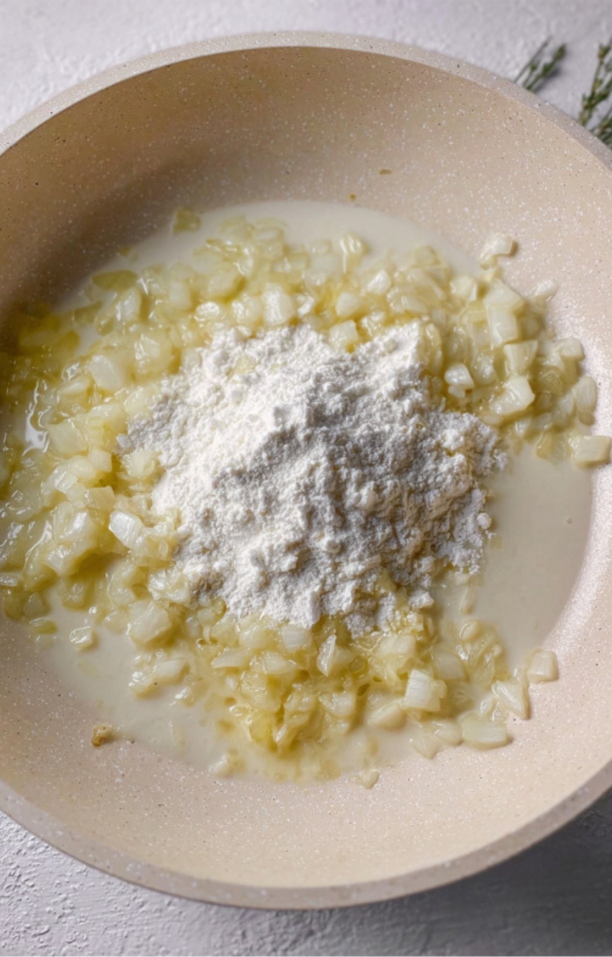 Diced onions sautéing in a pan with a mound of white flour on top to create a thickener for the pot pie sauce.