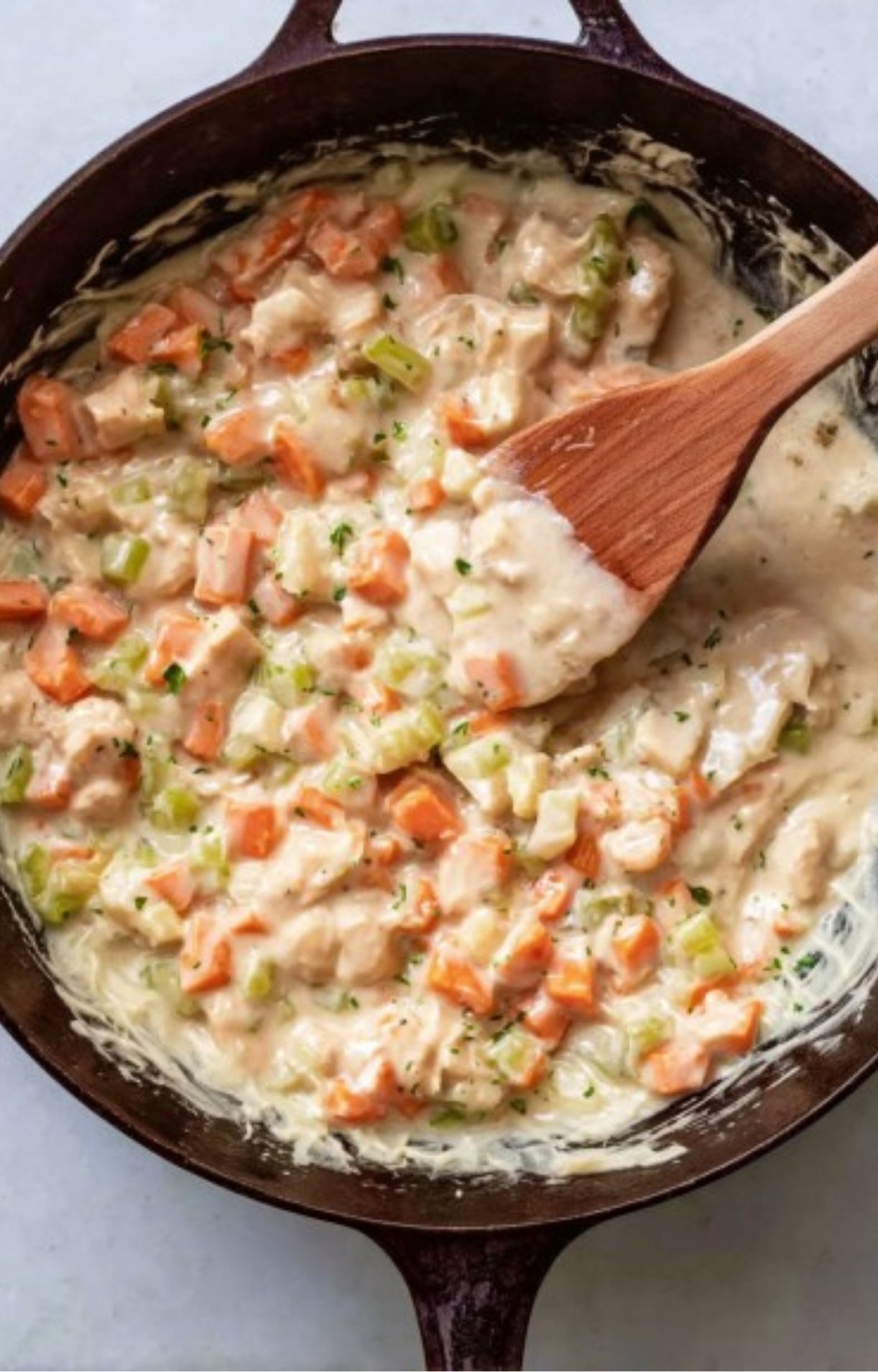 A thick, creamy white sauce covering carrots and celery in a skillet, representing the base of the Turkey Pot Pie with Puff Pastry.