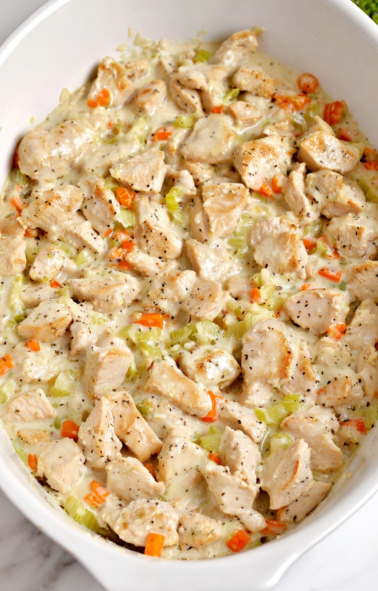 A prepared mixture of turkey, carrots, and celery in a thick cream sauce spread evenly in a white baking dish for a keto turkey pot pie.