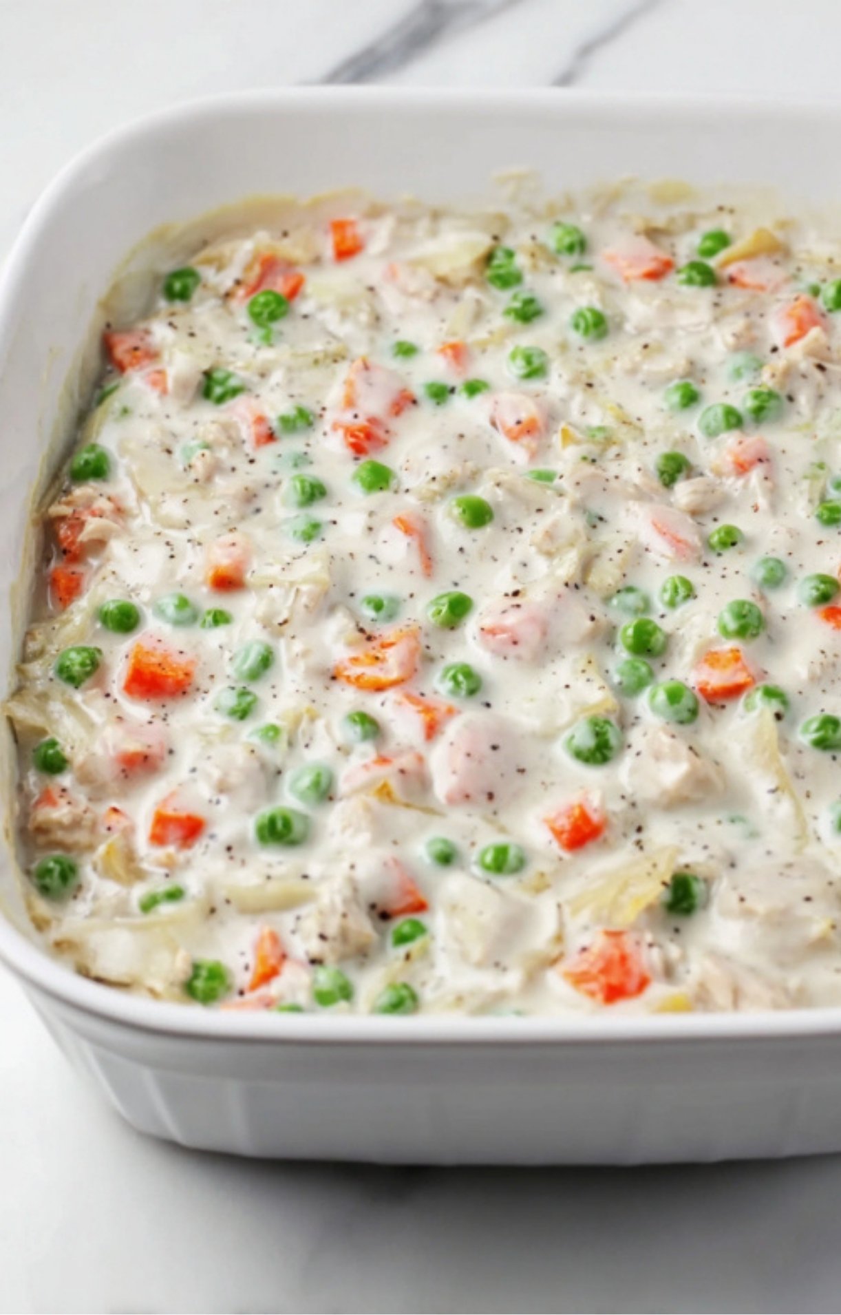 The turkey and vegetable creamy filling spread evenly into a white ceramic rectangular baking dish.