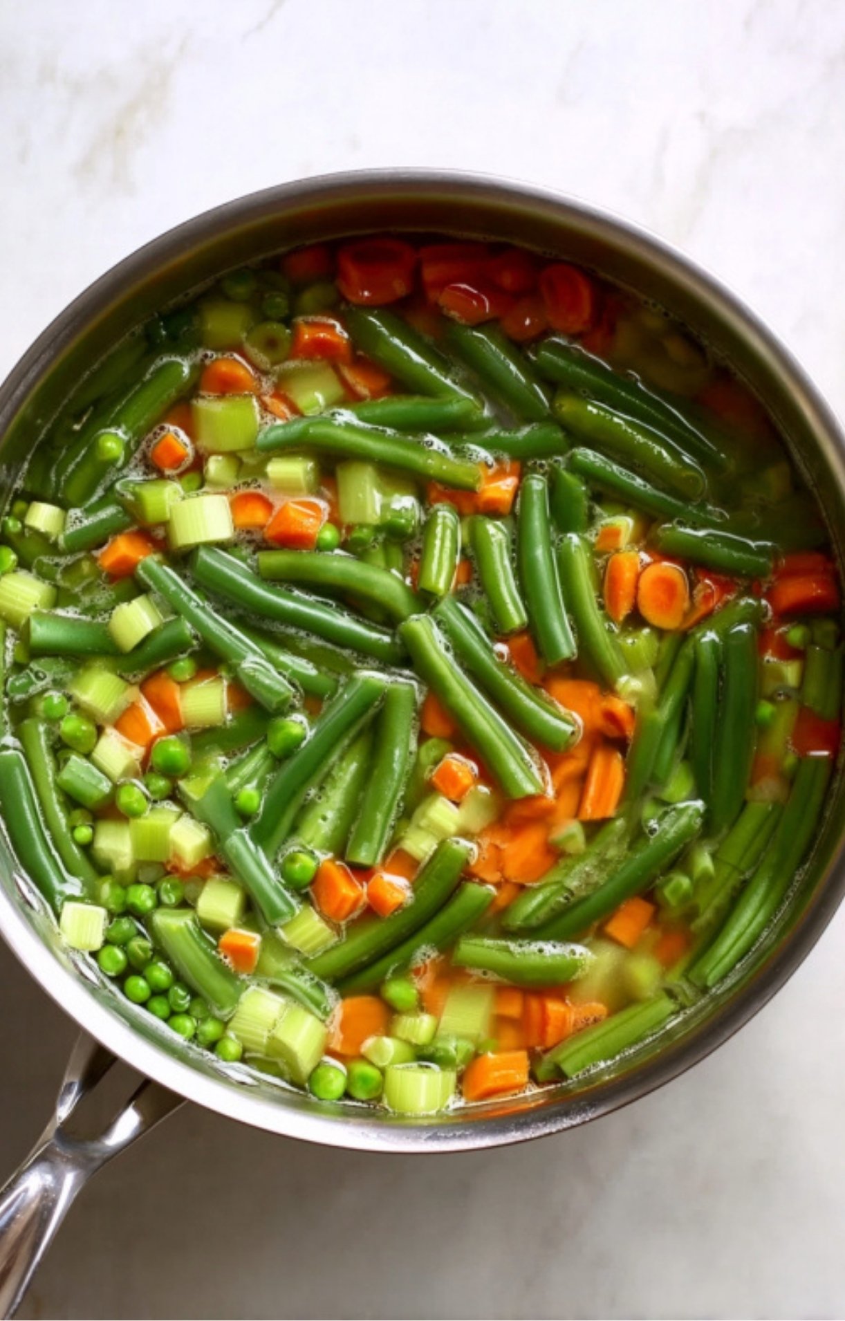 A pot filled with green beans, carrots, peas, and celery simmering in water to prepare the filling for Dad’s Turkey Pot Pie.