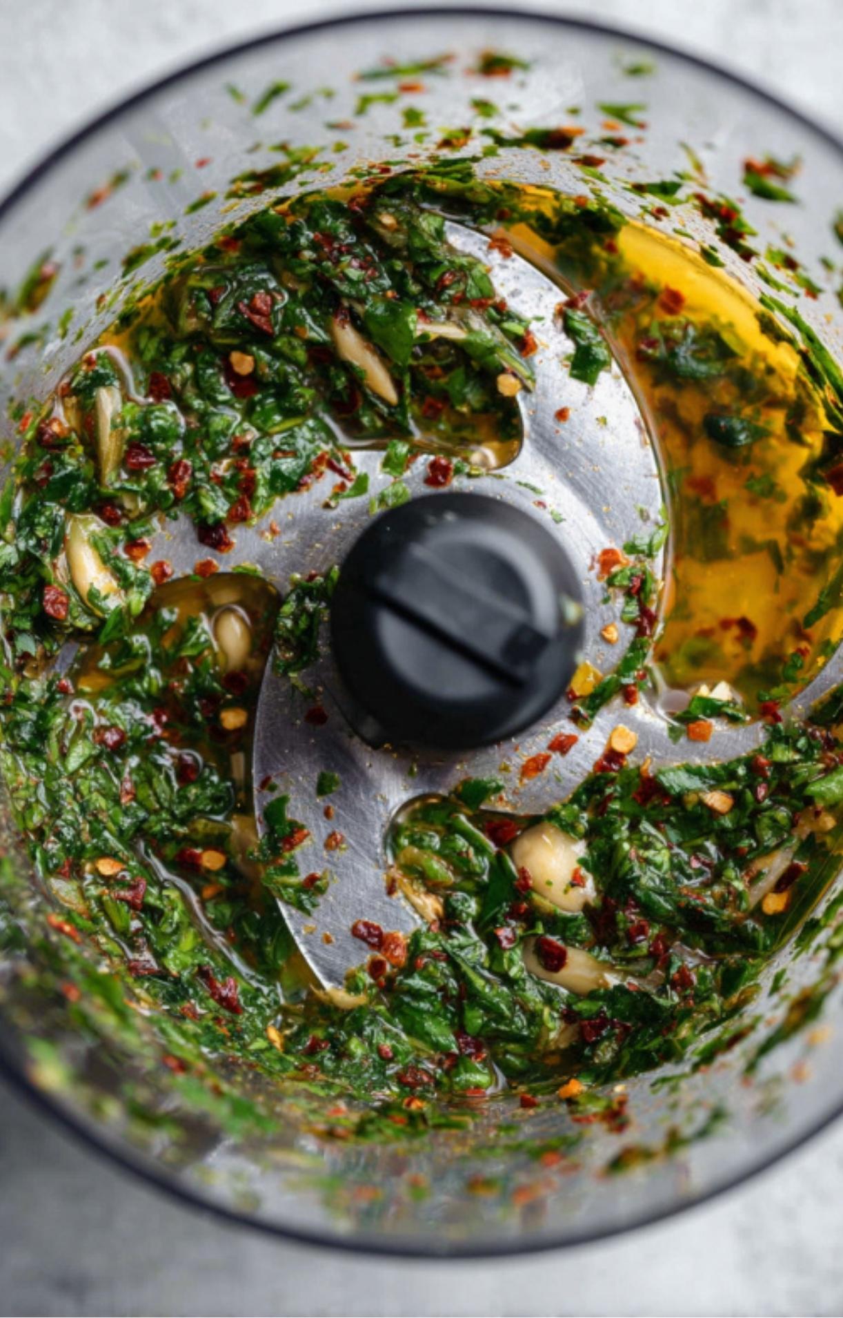 Fresh parsley, garlic, and red chili flakes being pulsed in a food processor with olive oil.