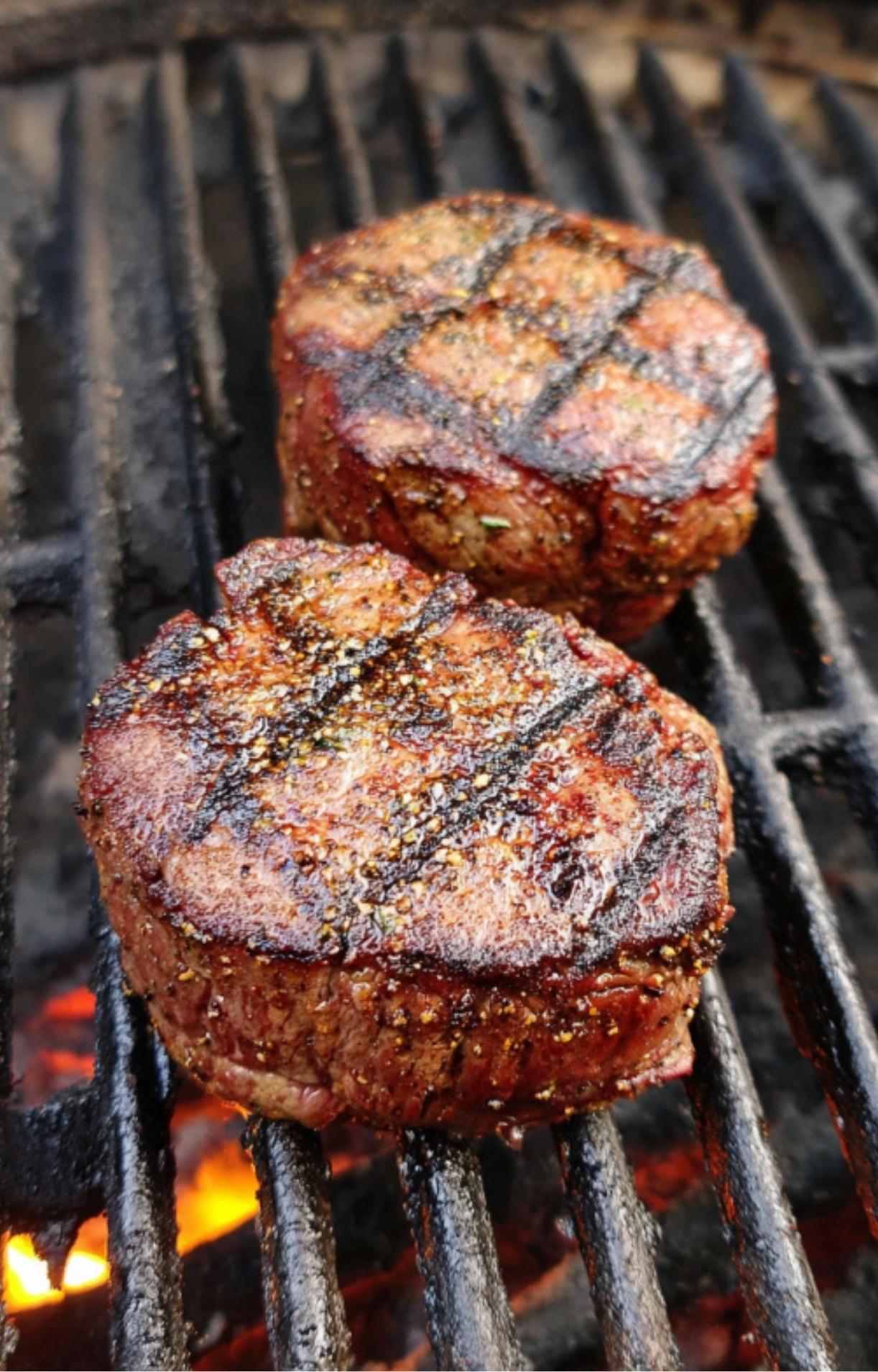 Two filet steaks with dark grill marks, perfectly cooked over open flames on a grill.