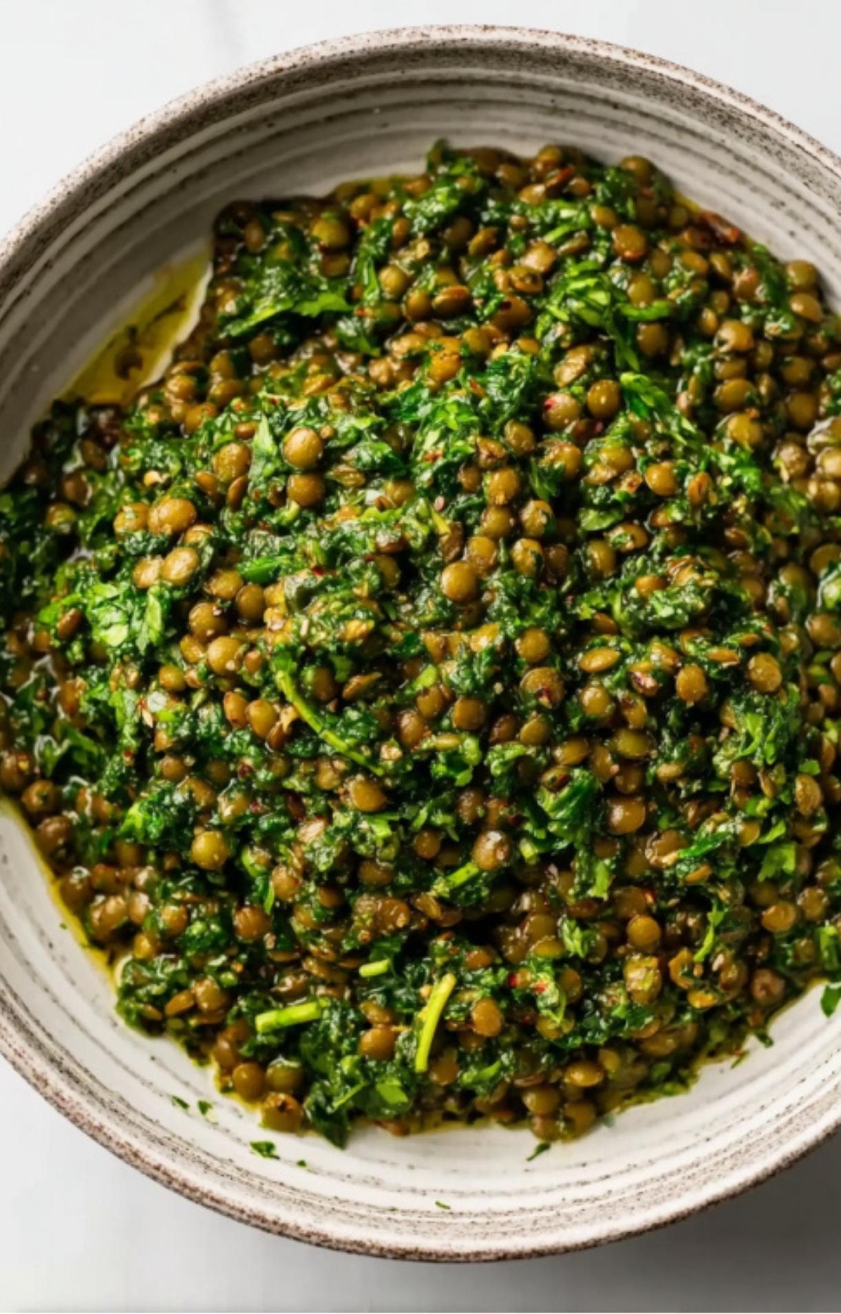 A bowl of green lentils mixed together with bright green chimichurri sauce.