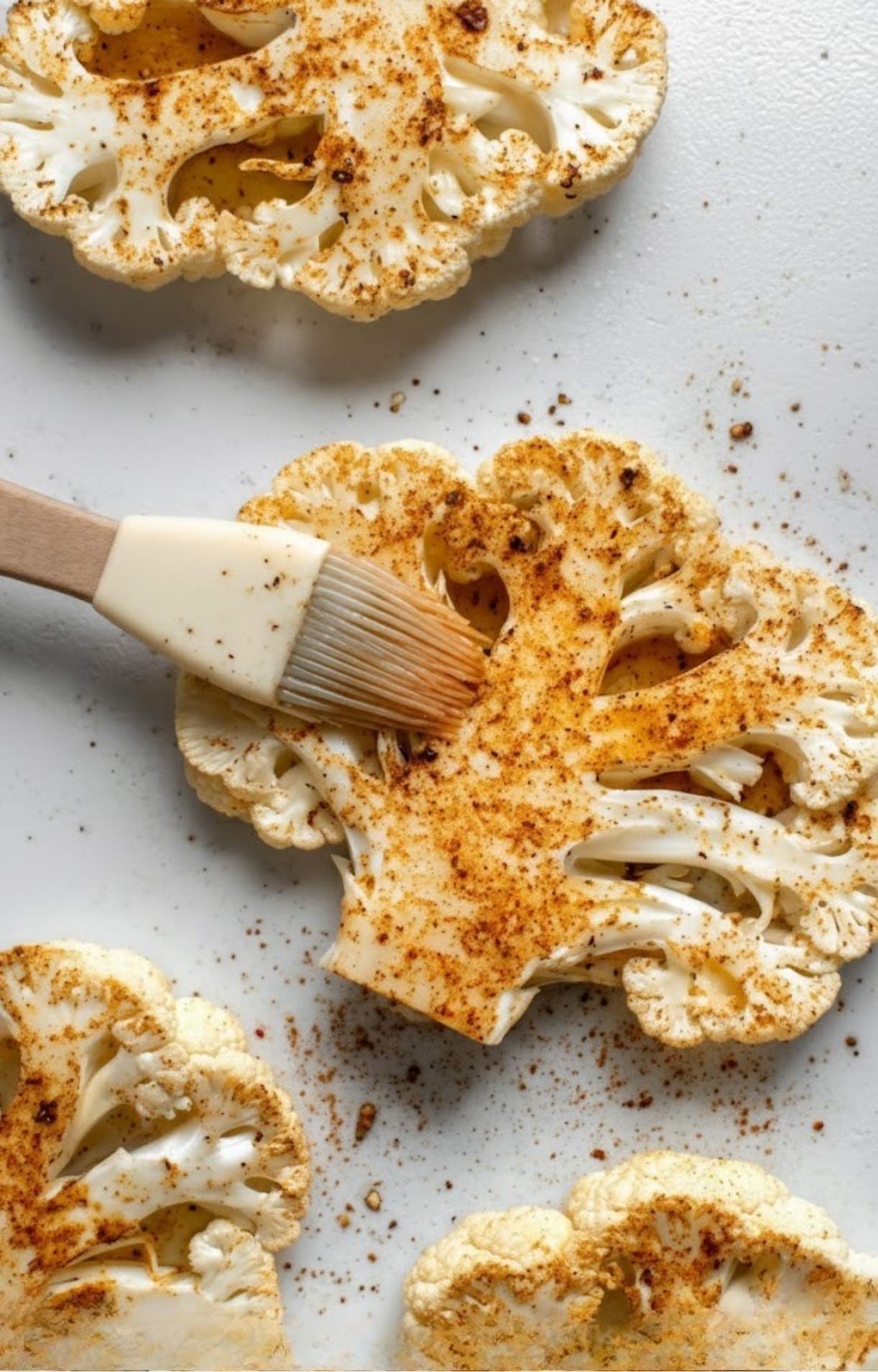 Sliced cauliflower steaks being brushed with a golden spice mixture, getting ready to be roasted or grilled.