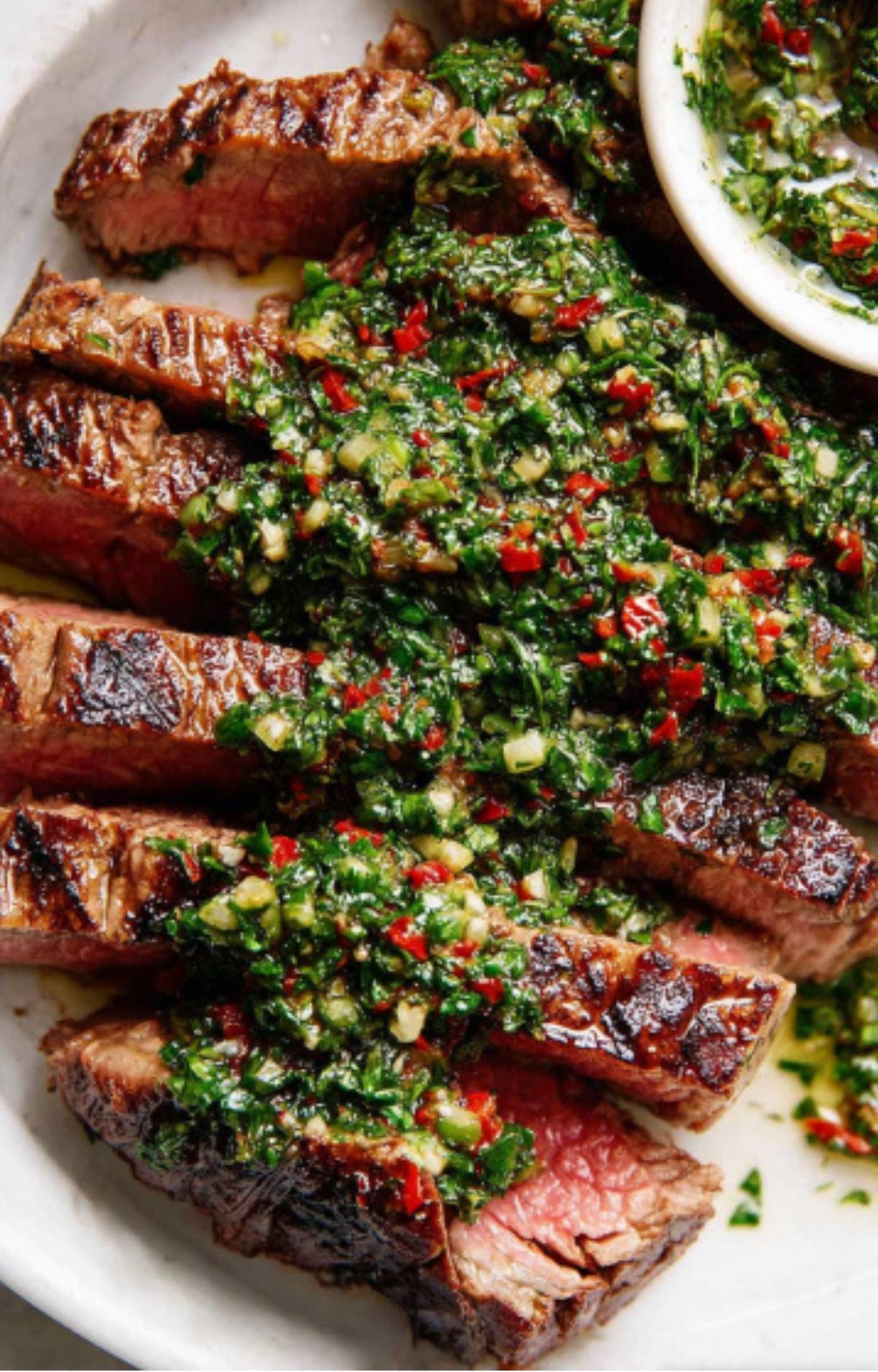 Sliced grilled steak generously topped with chunky green chimichurri sauce. Quick steak dinner idea for family meals and outdoor cooking.