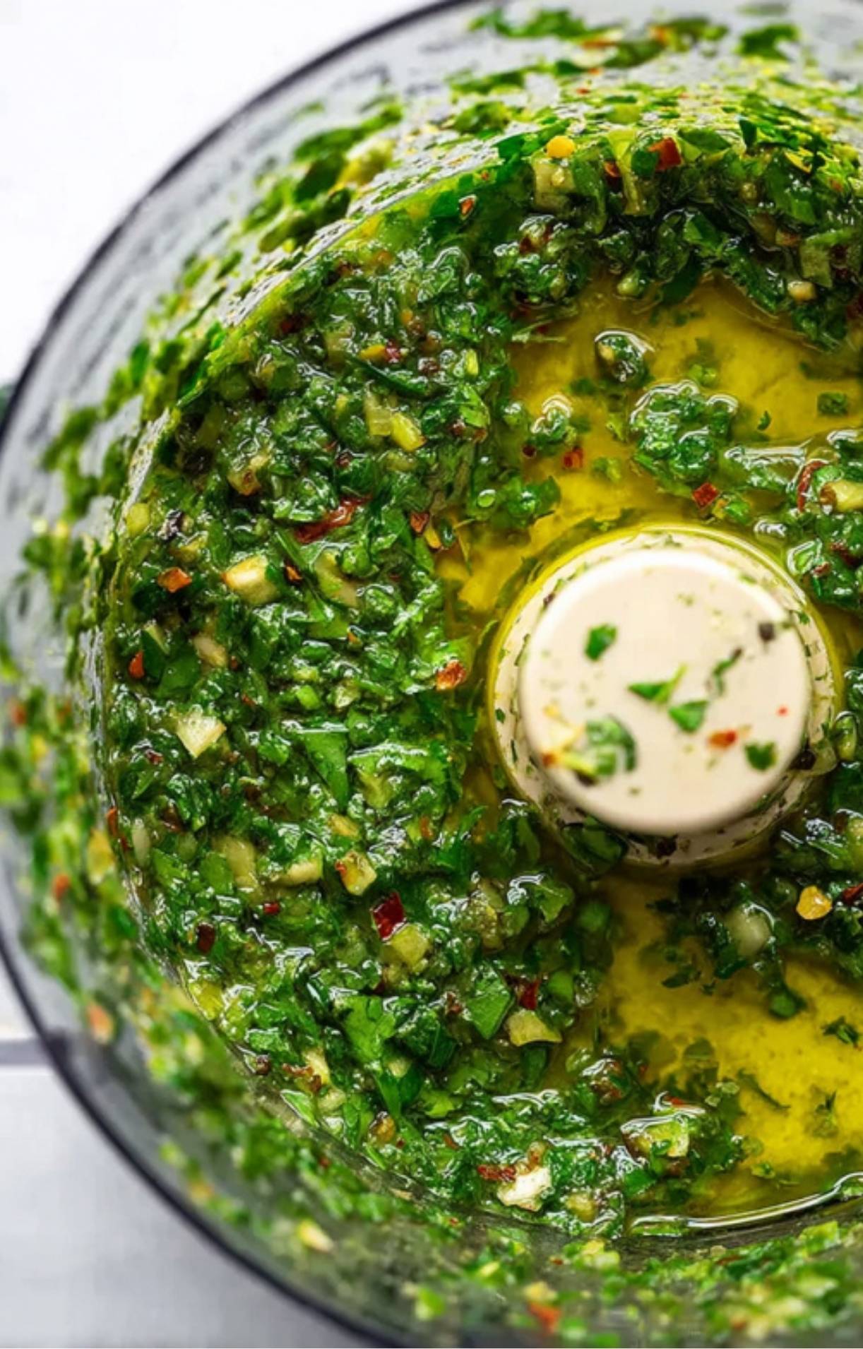 Close-up of blended green avocado chimichurri sauce in a food processor. Full of fresh herbs, olive oil, and chili for bold flavor.