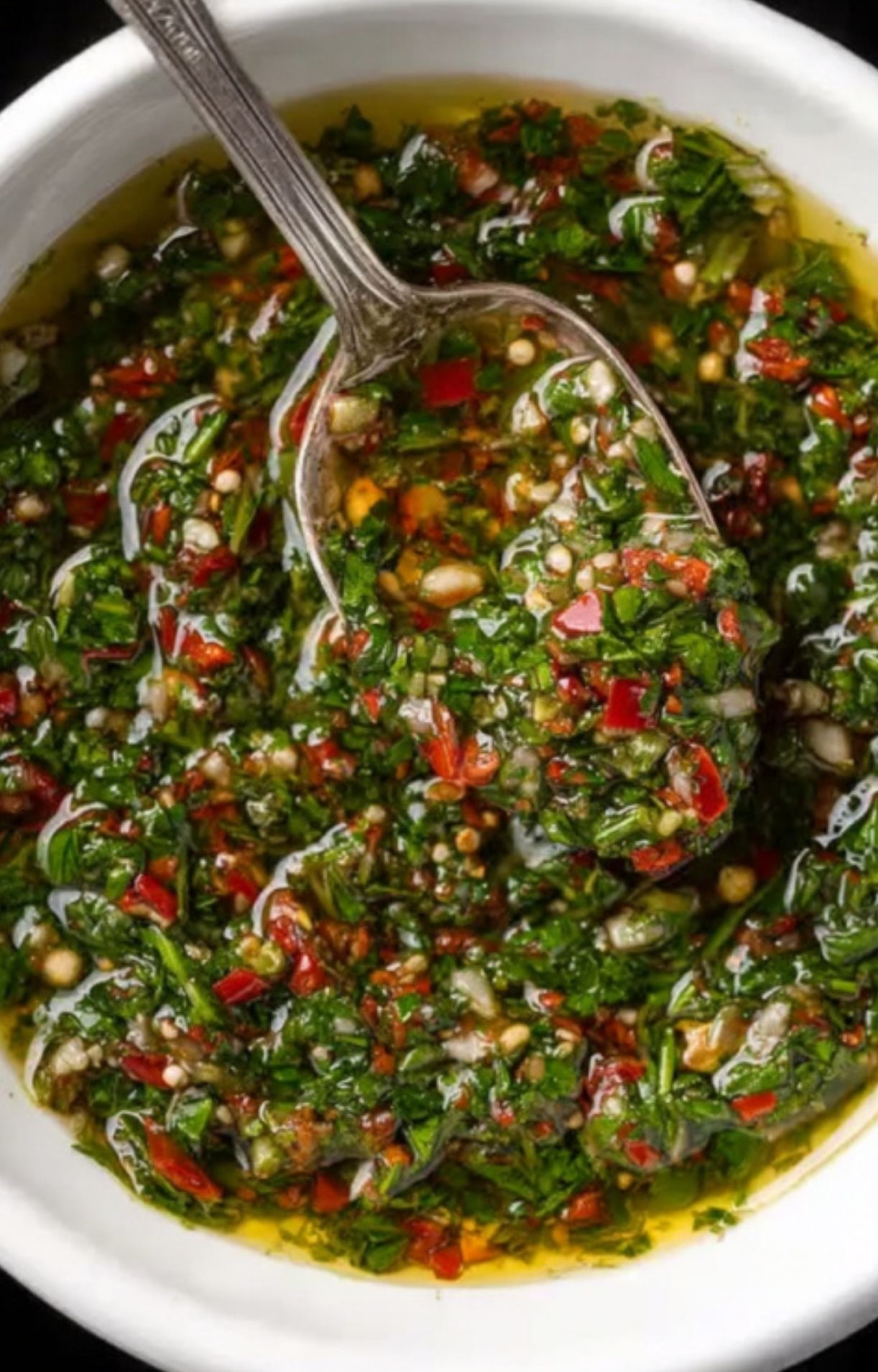 Bowl of vibrant green chimichurri sauce with red pepper flakes, parsley, and olive oil, ready to serve.