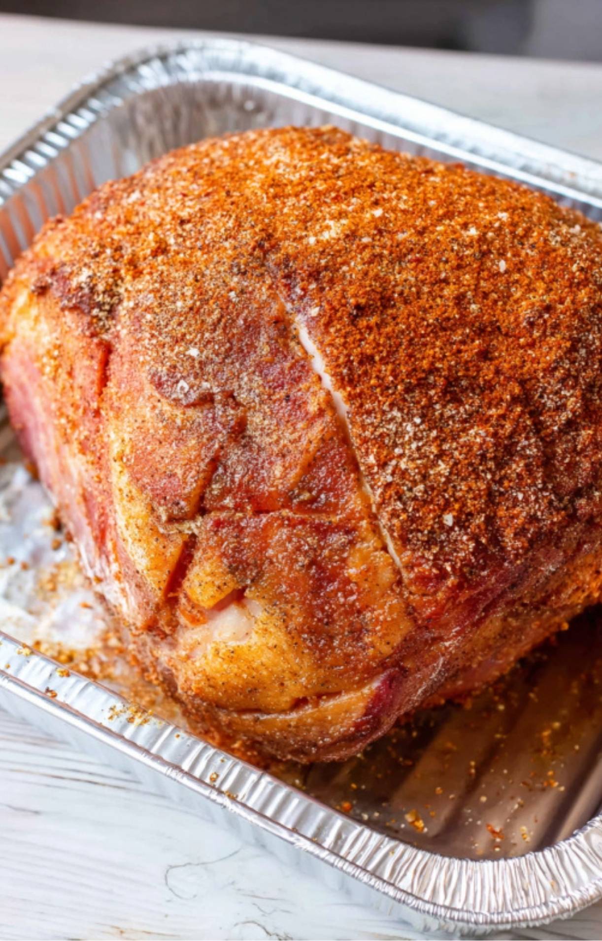 Ham coated with BBQ rub in a foil pan, ready to go on the grill for double smoking.