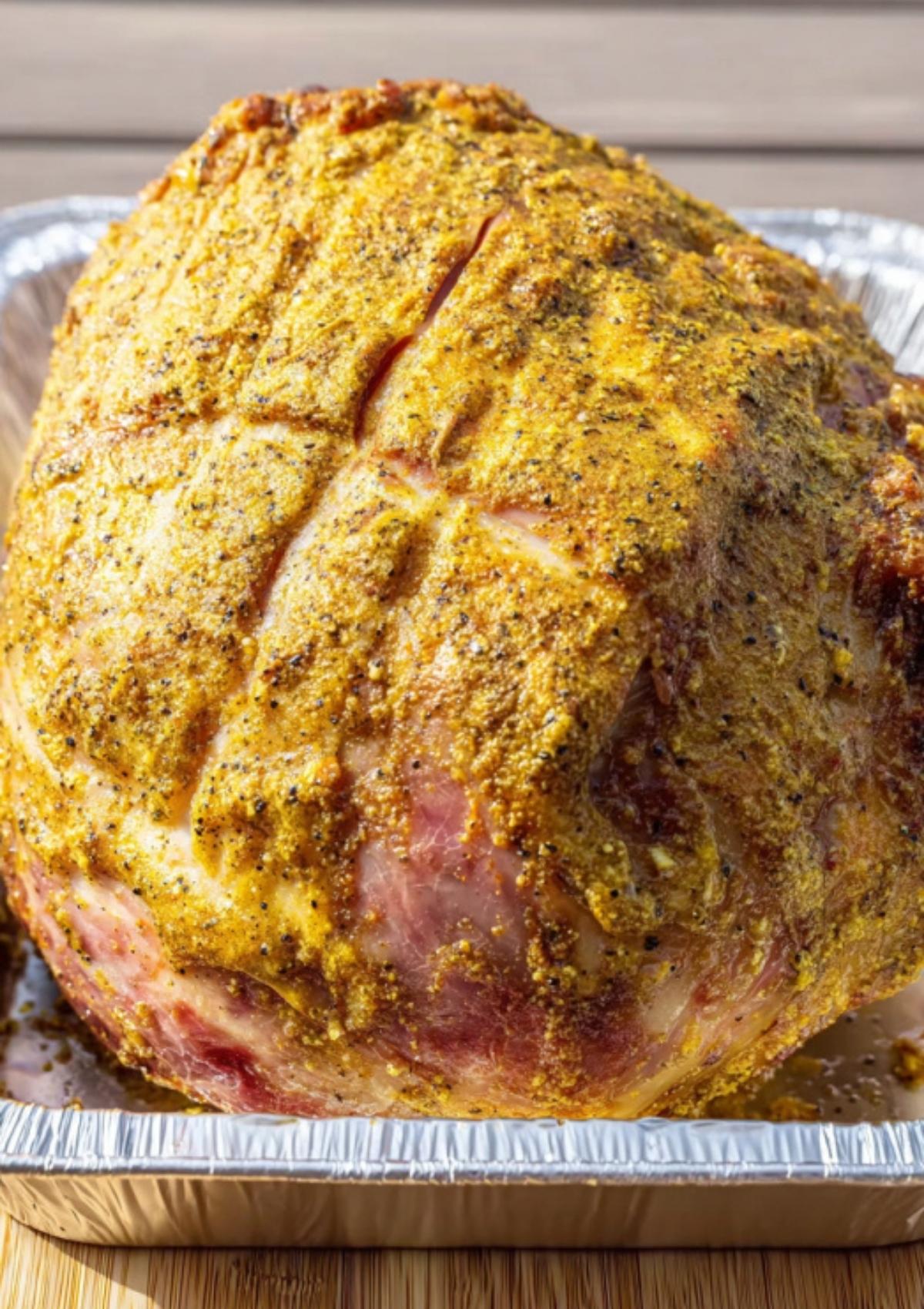 Ham covered in mustard rub ready to smoke for juicy holiday dinner