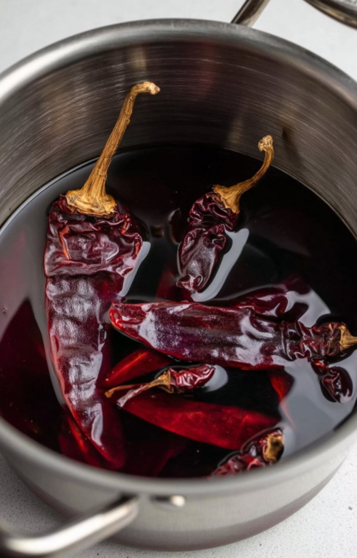 Several dried dark red chili peppers soaking in a pot of water to soften for the birria sauce.