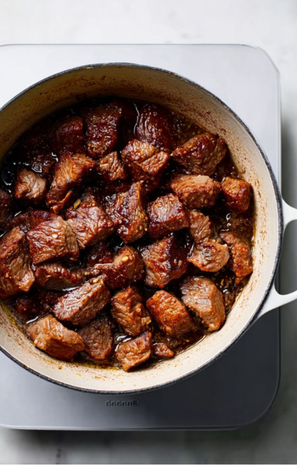 Cubes of beef chuck or brisket searing in a pot, coated in a dark, savory spice rub and juices.