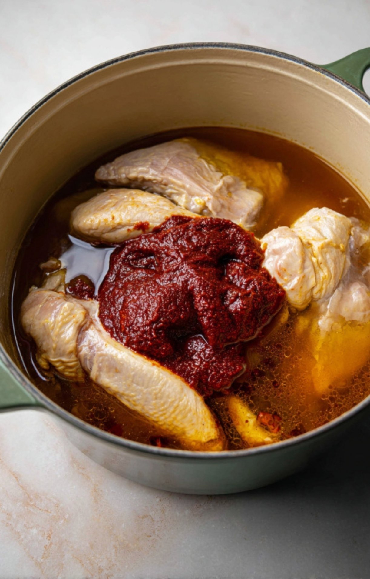 Adding a thick red chili paste to the pot of chicken and broth to create the birria base.