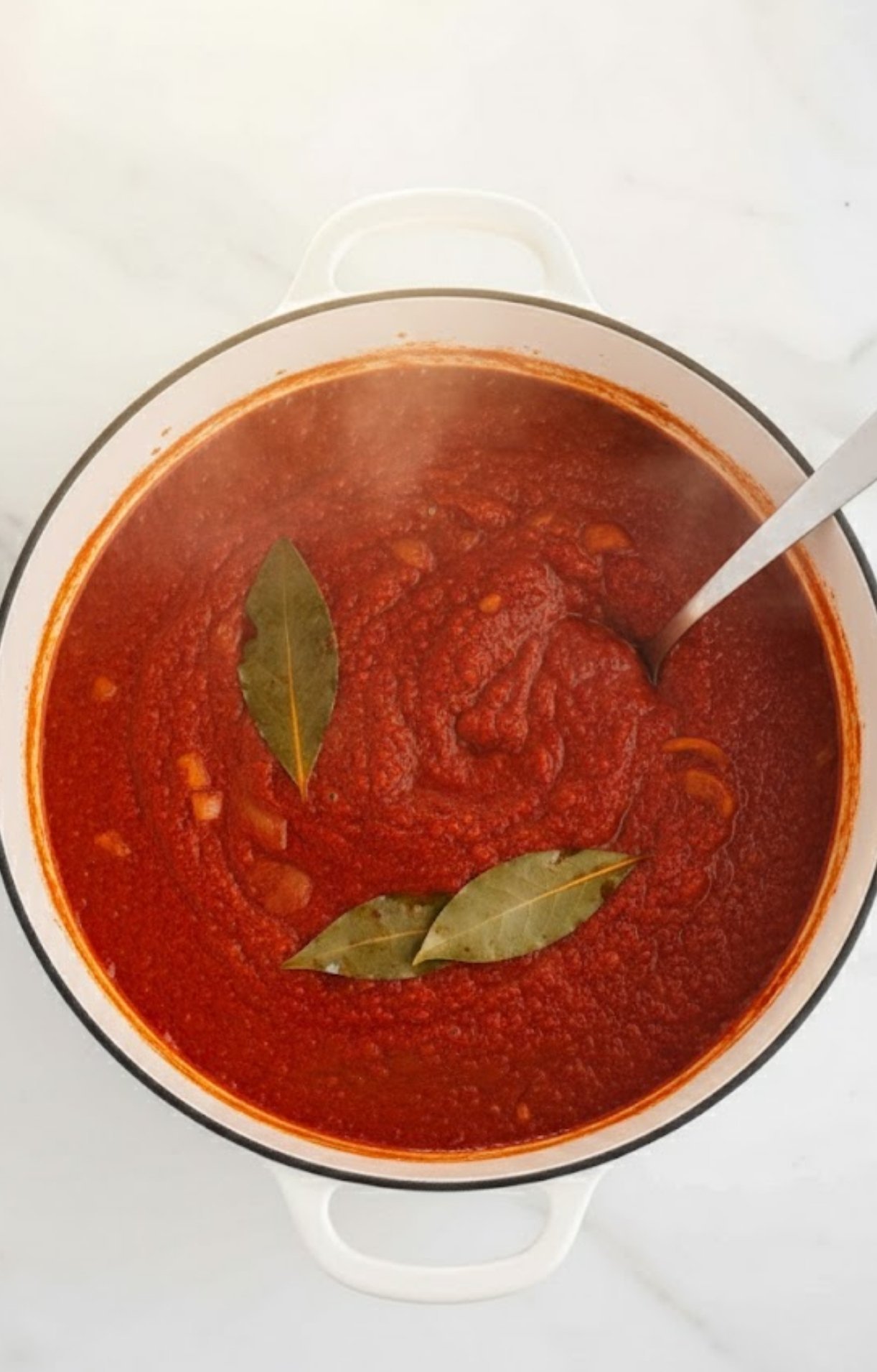 Close-up of a simmering pot of red chili broth with bay leaves, showing a thick and savory consistency.