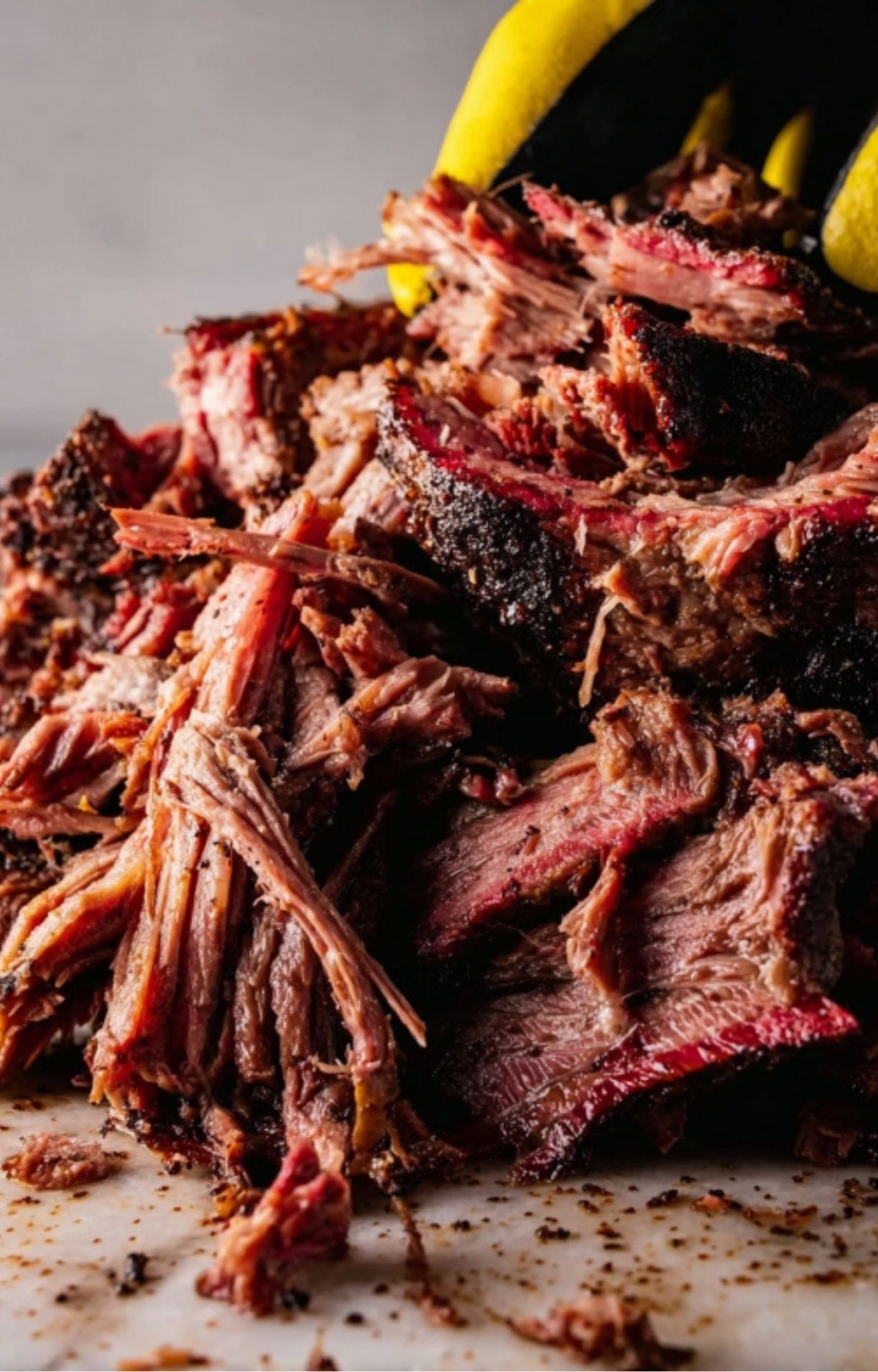 Close-up of tender, juicy smoked beef being pulled apart into shreds, showing a dark bark and pink smoke ring.