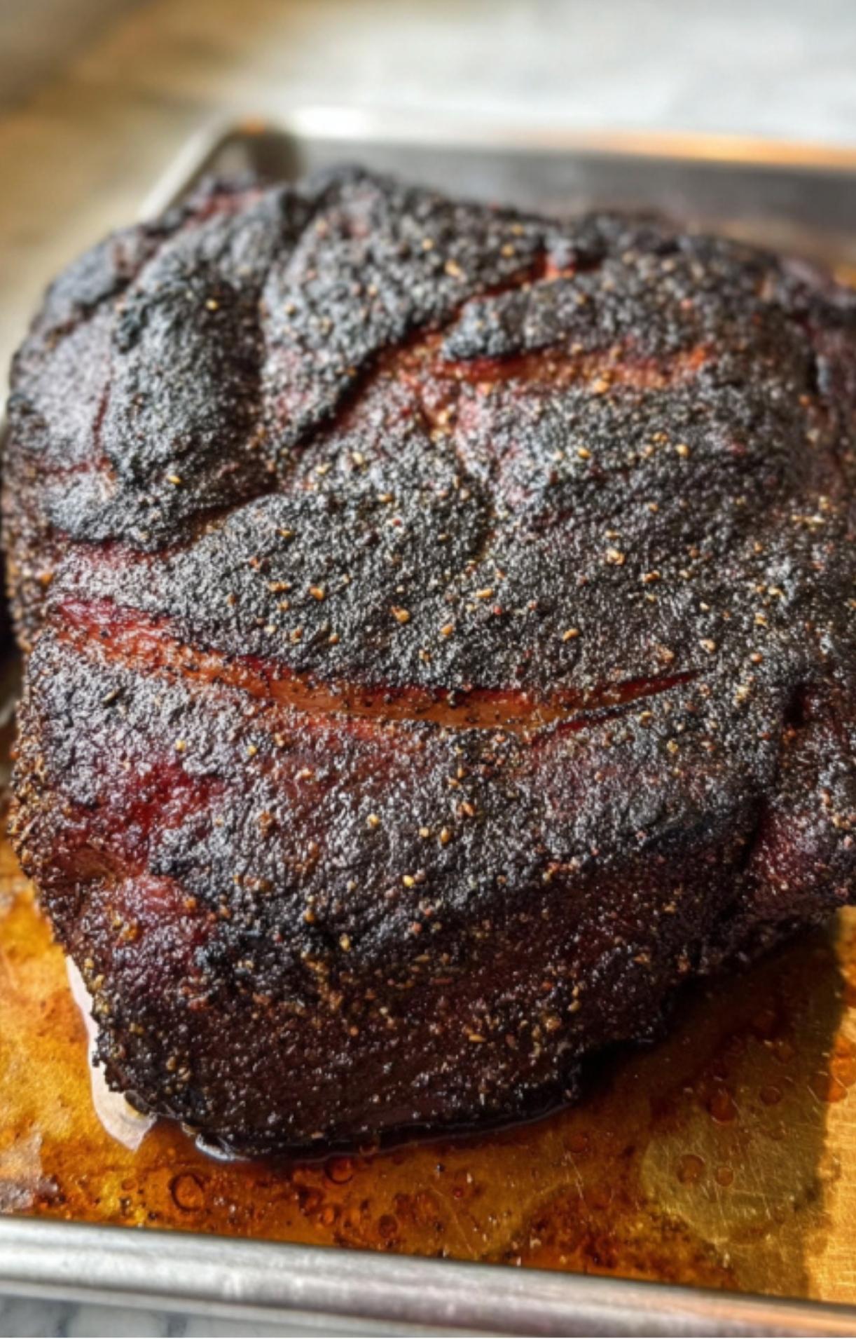 A whole beef chuck roast after smoking, featuring a dark, crusty black bark and resting on a metal baking sheet.