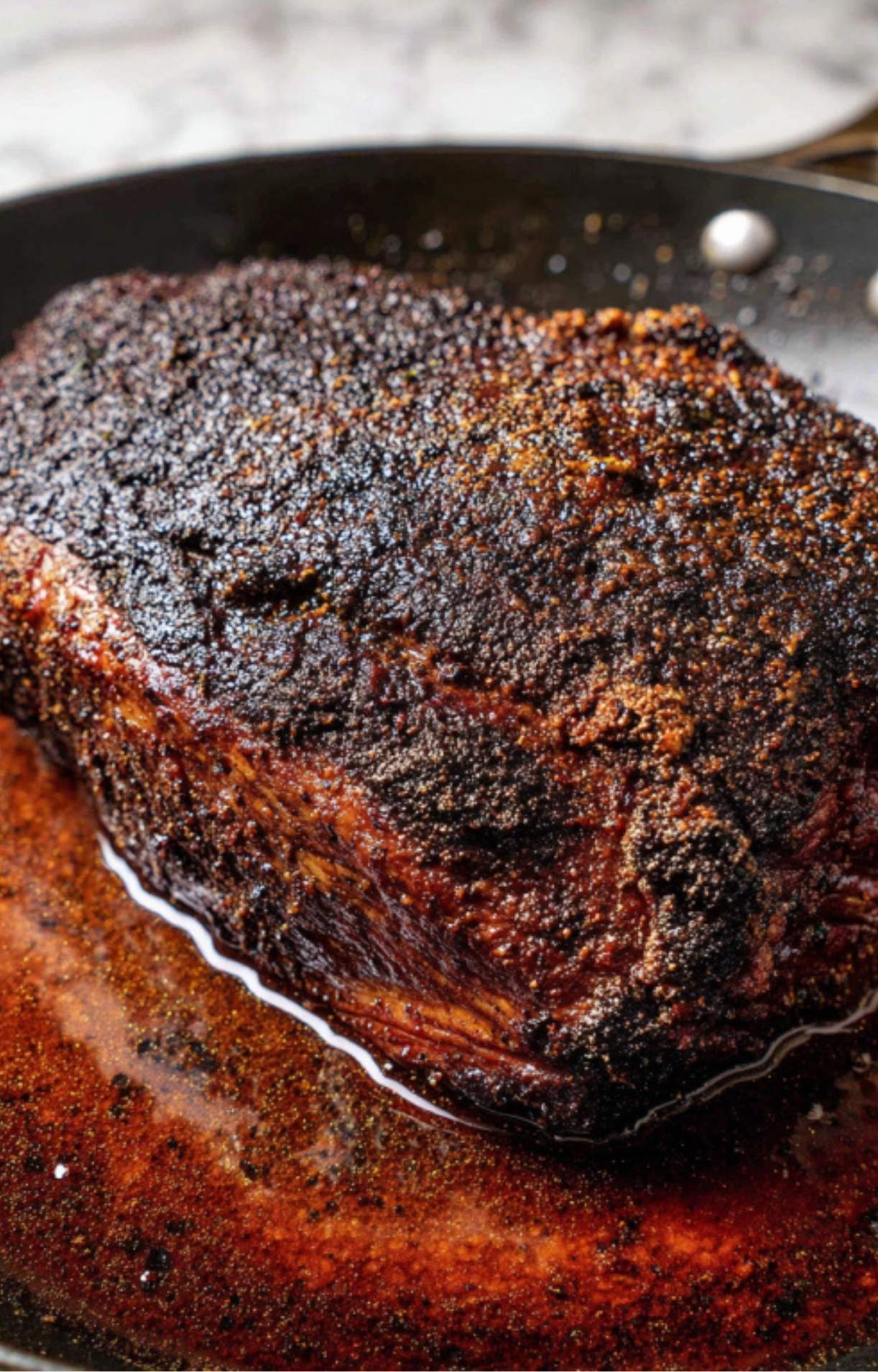 A large beef chuck roast with a dark, flavorful spice crust being seared in a hot skillet to lock in juices.