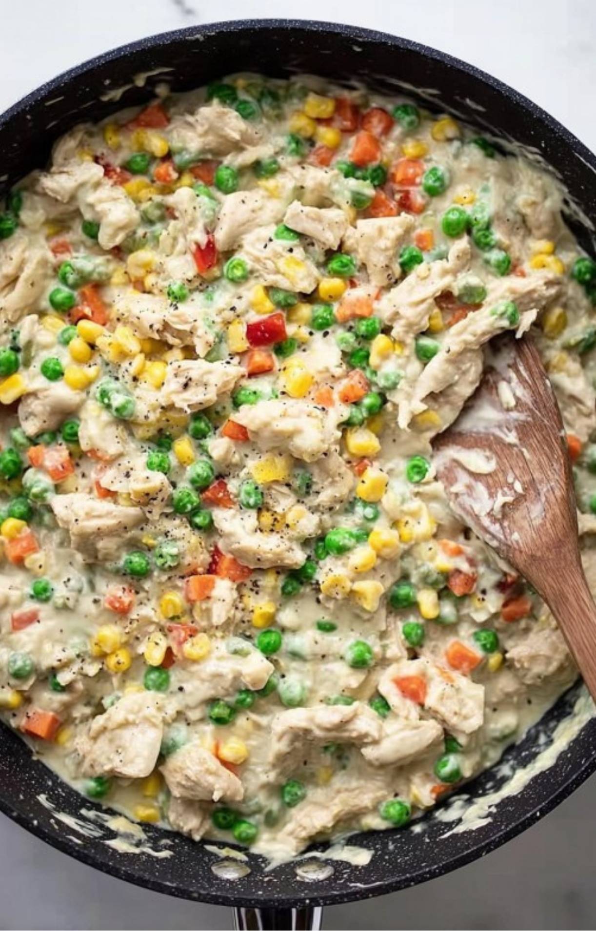 Shreddred turkey, bright green peas, and yellow corn being stirred into the thick, creamy sauce mixture.