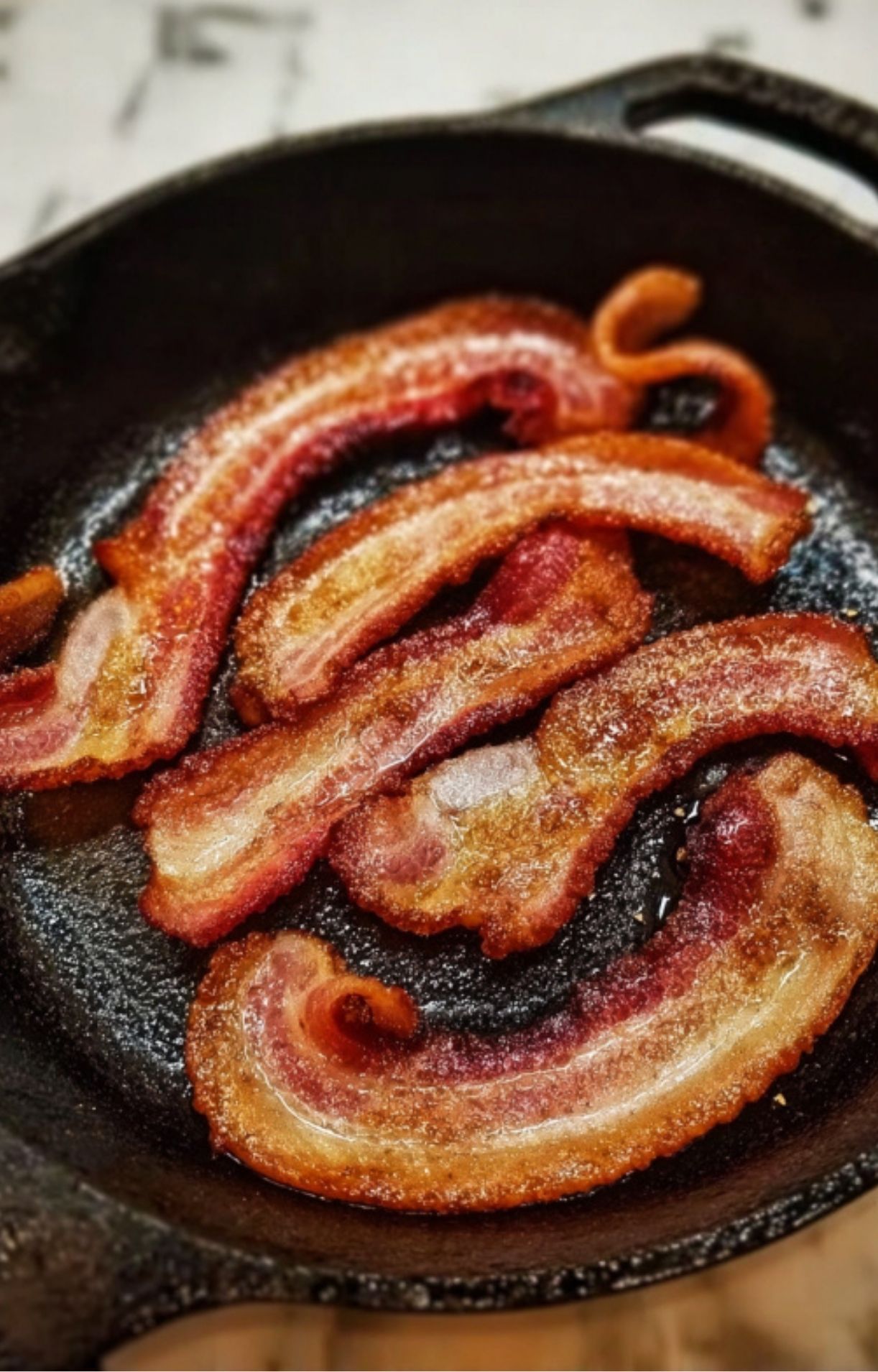 Several strips of bacon frying until golden and crispy in a black cast-iron skillet.